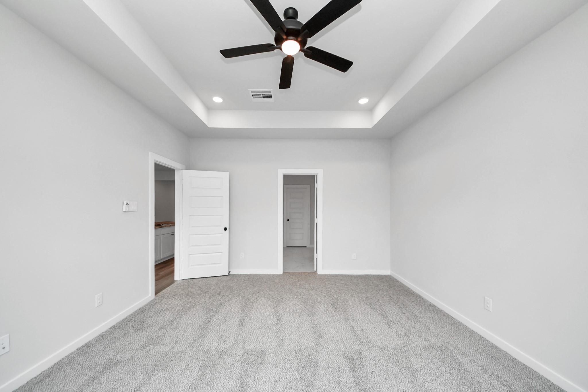 Spacious bedroom with tray ceiling and ceiling fan in The Everett C floor plan at River Ranch Meadows, Dayton, Texas.