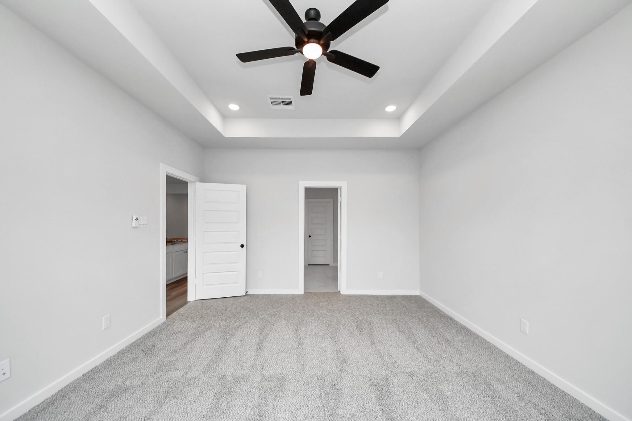 Spacious bedroom with tray ceiling and ceiling fan in The Everett C floor plan at River Ranch Meadows, Dayton, Texas.