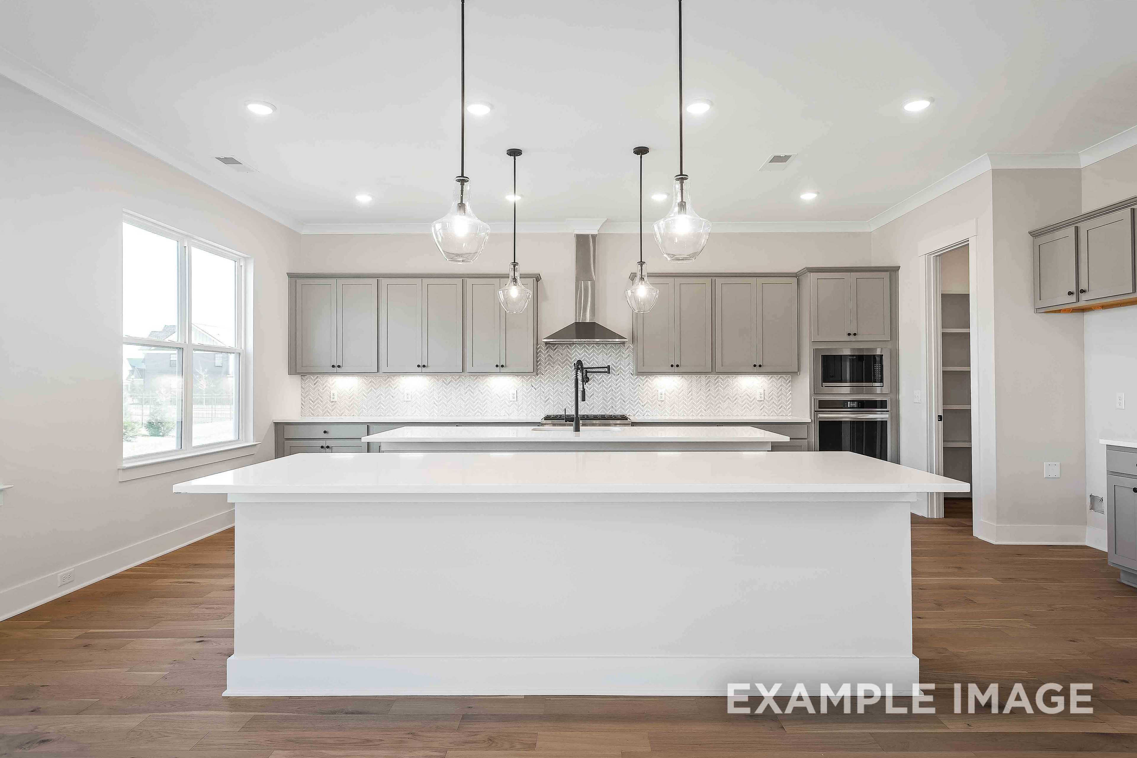 Spacious kitchen in The Alston A featuring large white island, gray shaker cabinets, stainless steel appliances, and pendant lights