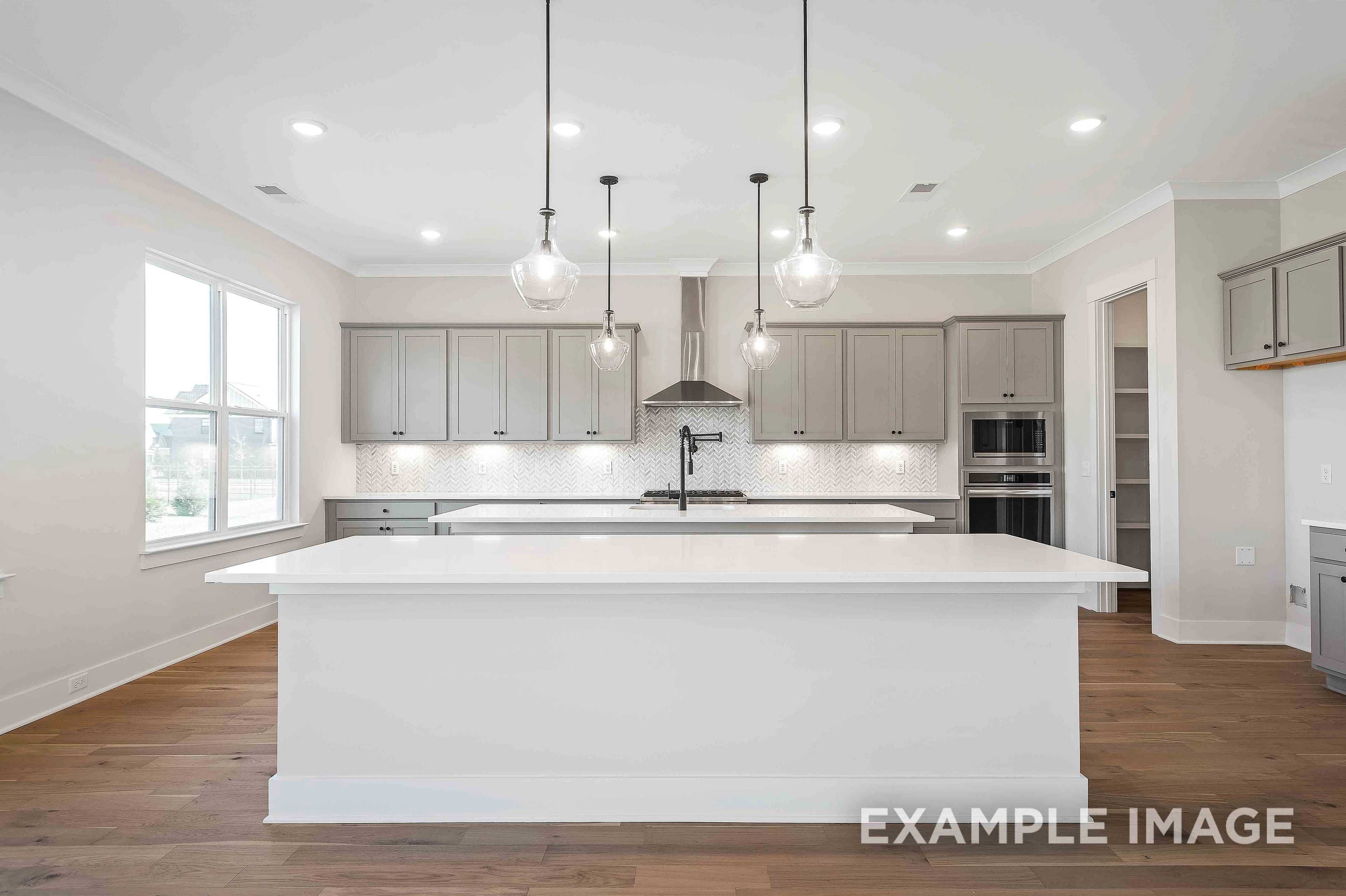 Spacious kitchen in The Alston A featuring large white island, gray shaker cabinets, stainless steel appliances, and pendant lights