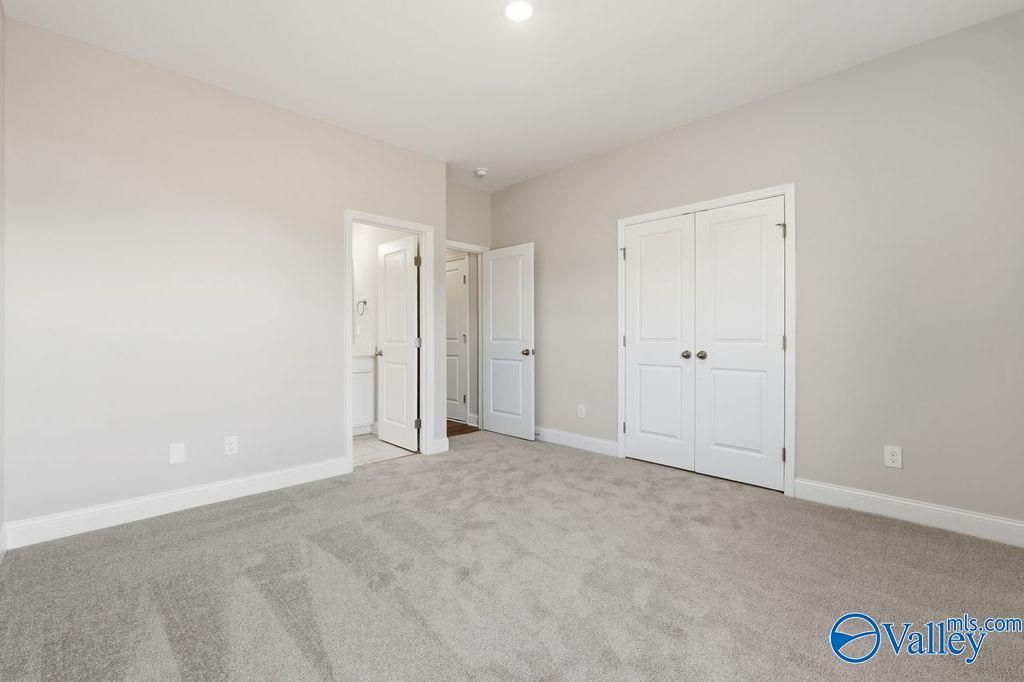 Spacious bedroom with beige walls, gray carpet, attached bath, and double-door closet in Davidson Homes The Harrison, Hartselle, AL