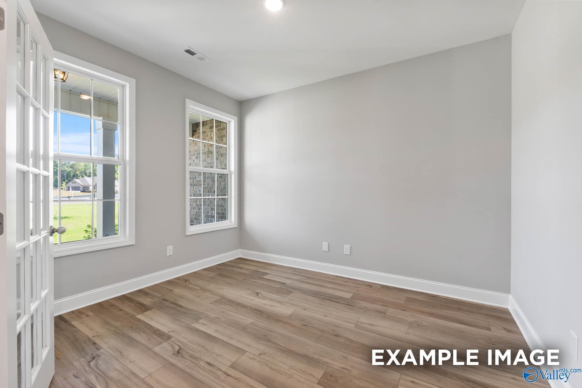 Bright secondary bedroom with gray walls, hardwood floors, and large grid windows overlooking lush yard in Davidson Homes The Rockford, Madison AL