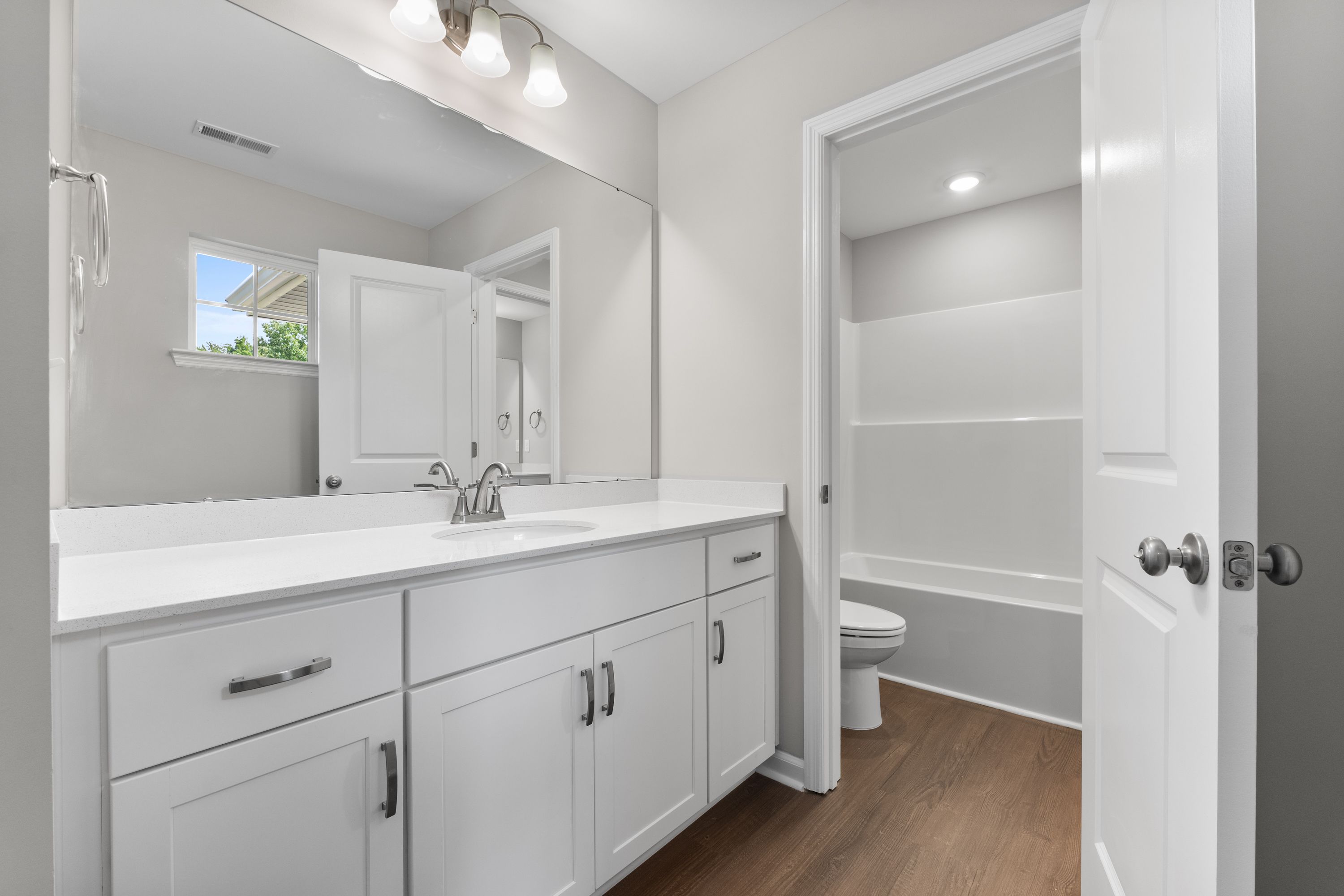 Spacious master bathroom in The Avalon E with white double vanity, large mirror, walk-in shower, soaking tub, and hardwood floors