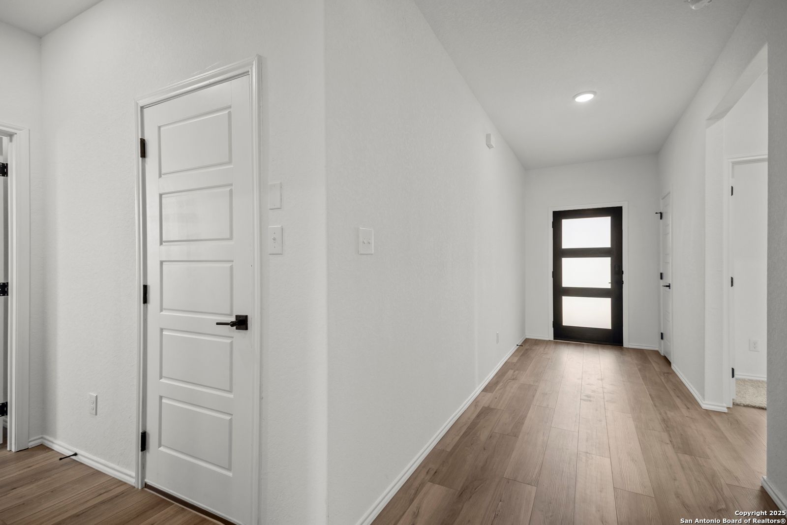 Bright hallway with white walls, hardwood floors, and glass-paneled door in 4-bedroom Davidson Homes The Daphne K, San Antonio, TX