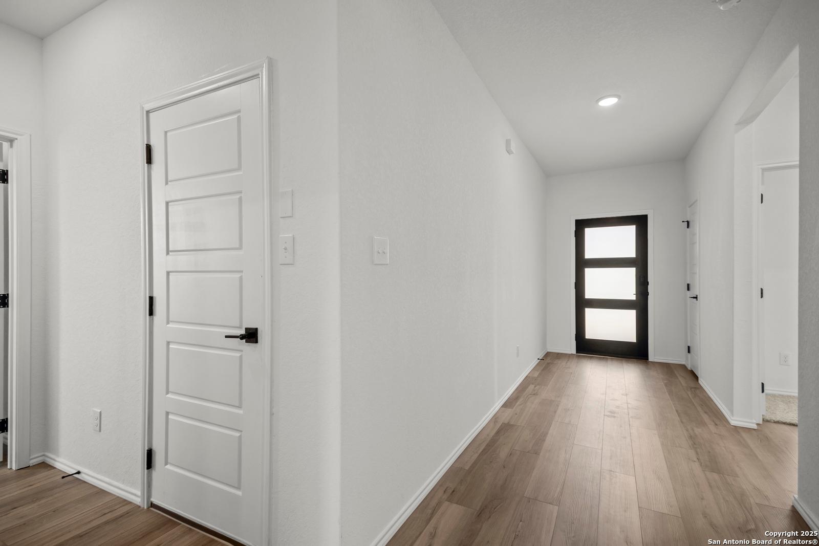 Bright hallway with white walls, hardwood floors, and glass-paneled door in 4-bedroom Davidson Homes The Daphne K, San Antonio, TX