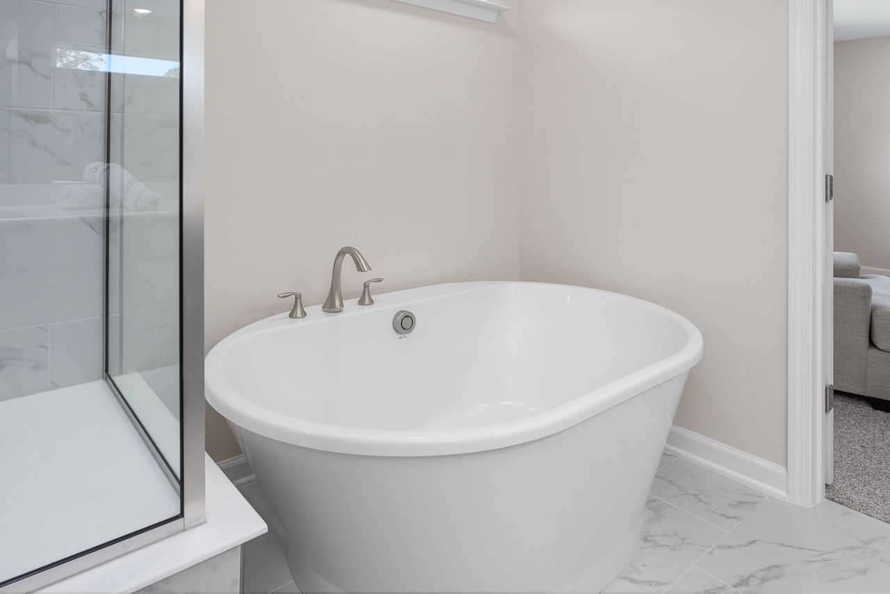 Modern soaking tub in the master suite of The Chestnut, featuring marble-style tile flooring and a glass-enclosed shower.