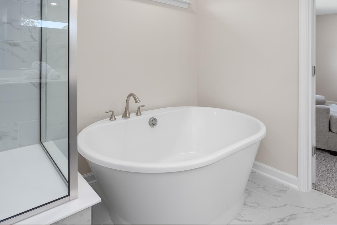 Modern soaking tub in the master suite of The Chestnut, featuring marble-style tile flooring and a glass-enclosed shower.