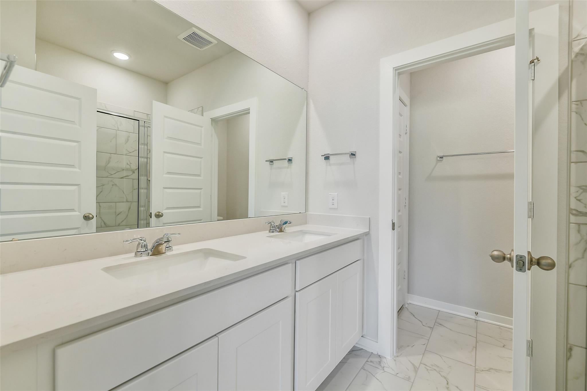 Modern master bathroom featuring double white vanity, quartz counters, marble shower, and closet in Davidson Homes San Marcos E, Conroe TX