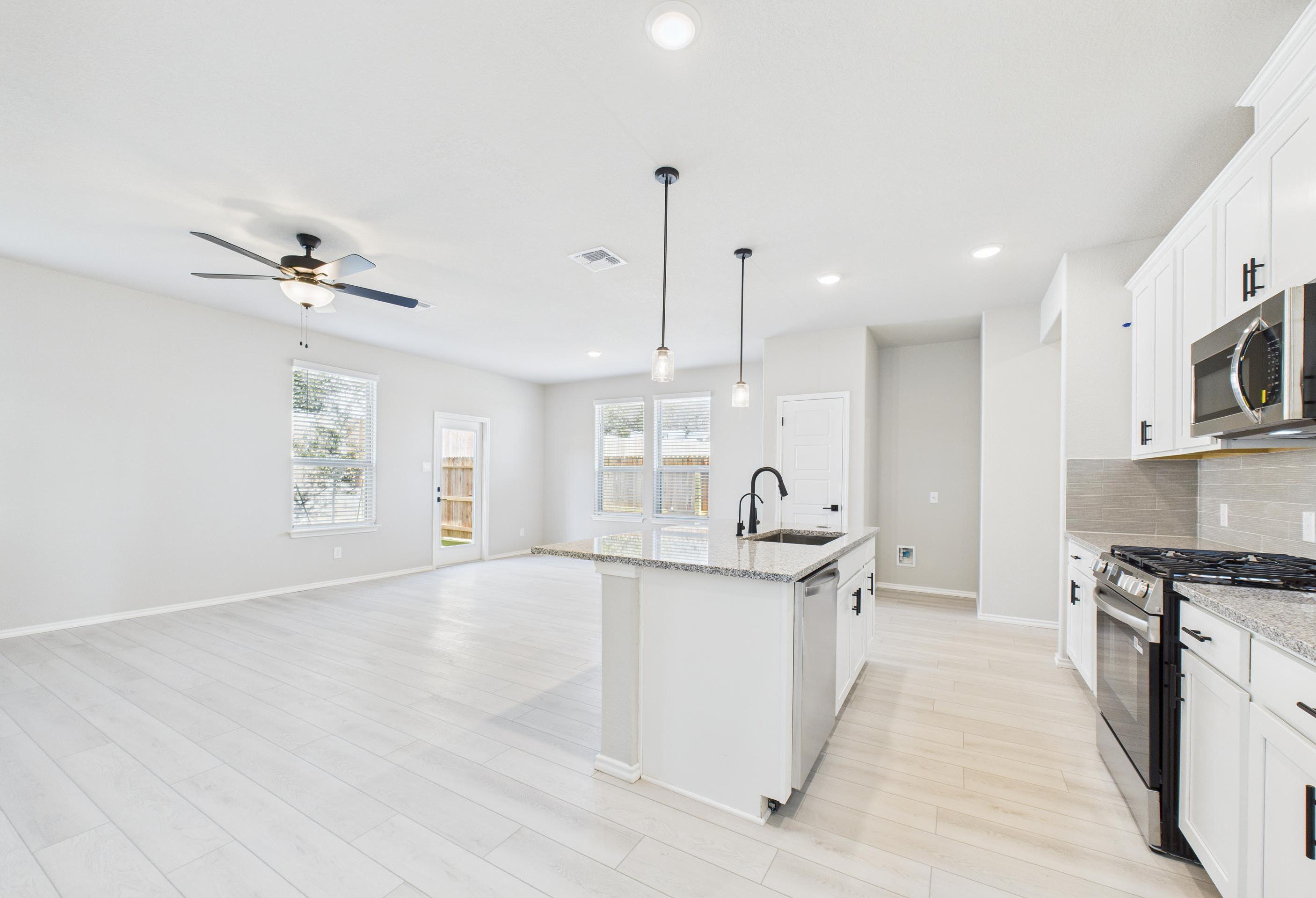 Open-concept kitchen and living area in The Charlotte A, featuring a large granite island and modern white cabinetry.