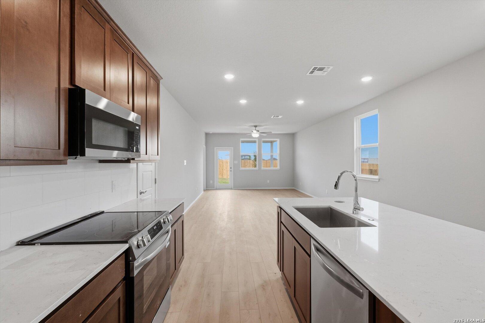 Modern open-concept kitchen with quartz counters, stainless appliances, and hardwood floors in Davidson Homes The Frio B, San Antonio