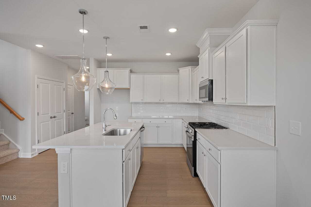 Modern white shaker kitchen with large island sink, stainless appliances, and pendant lights in Davidson Homes The Graham, Fuquay-Varina, NC