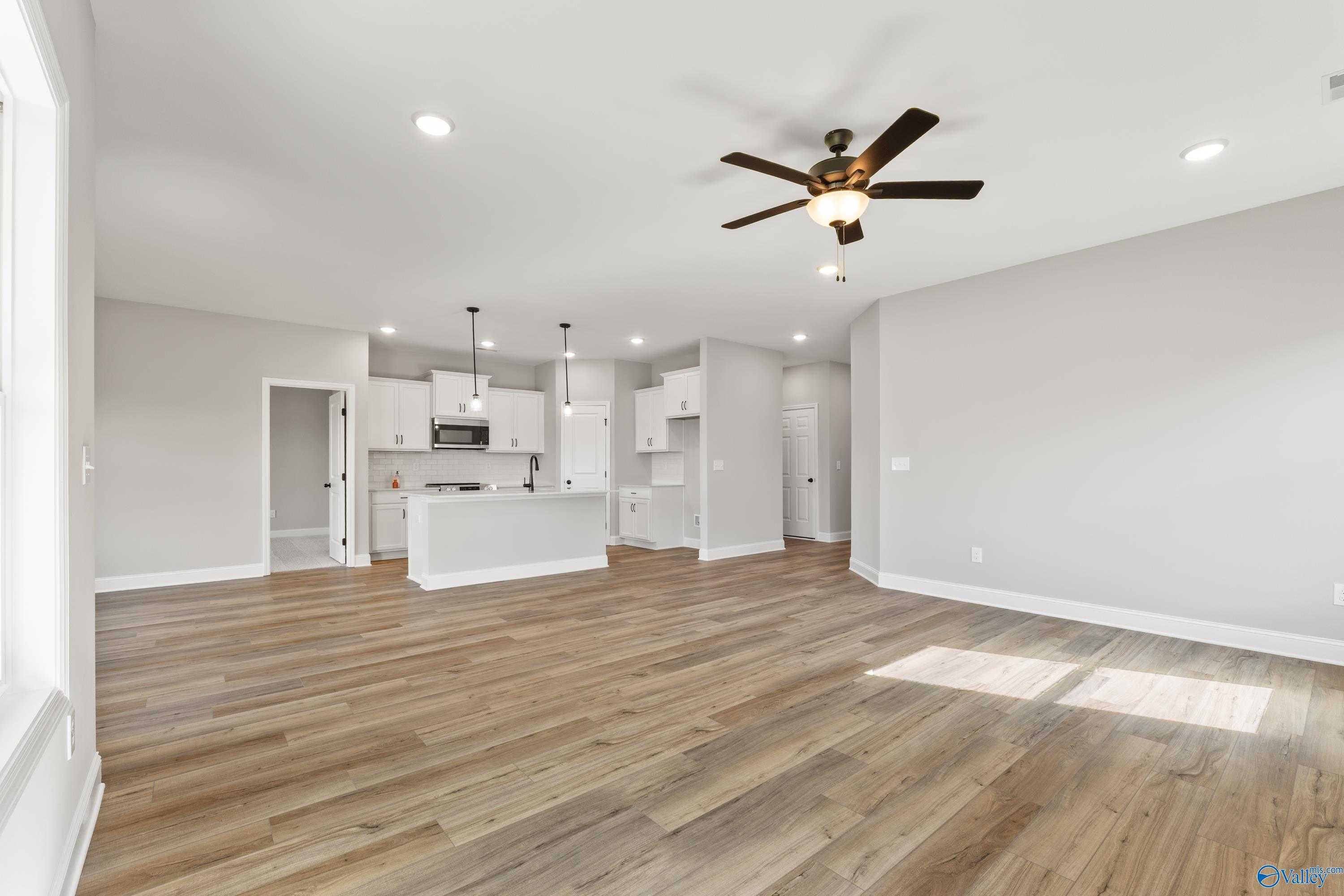 Open-concept kitchen and living area with white cabinets, island sink, ceiling fan, hardwood floors in Davidson Homes The Franklin B, Hazel Green, AL