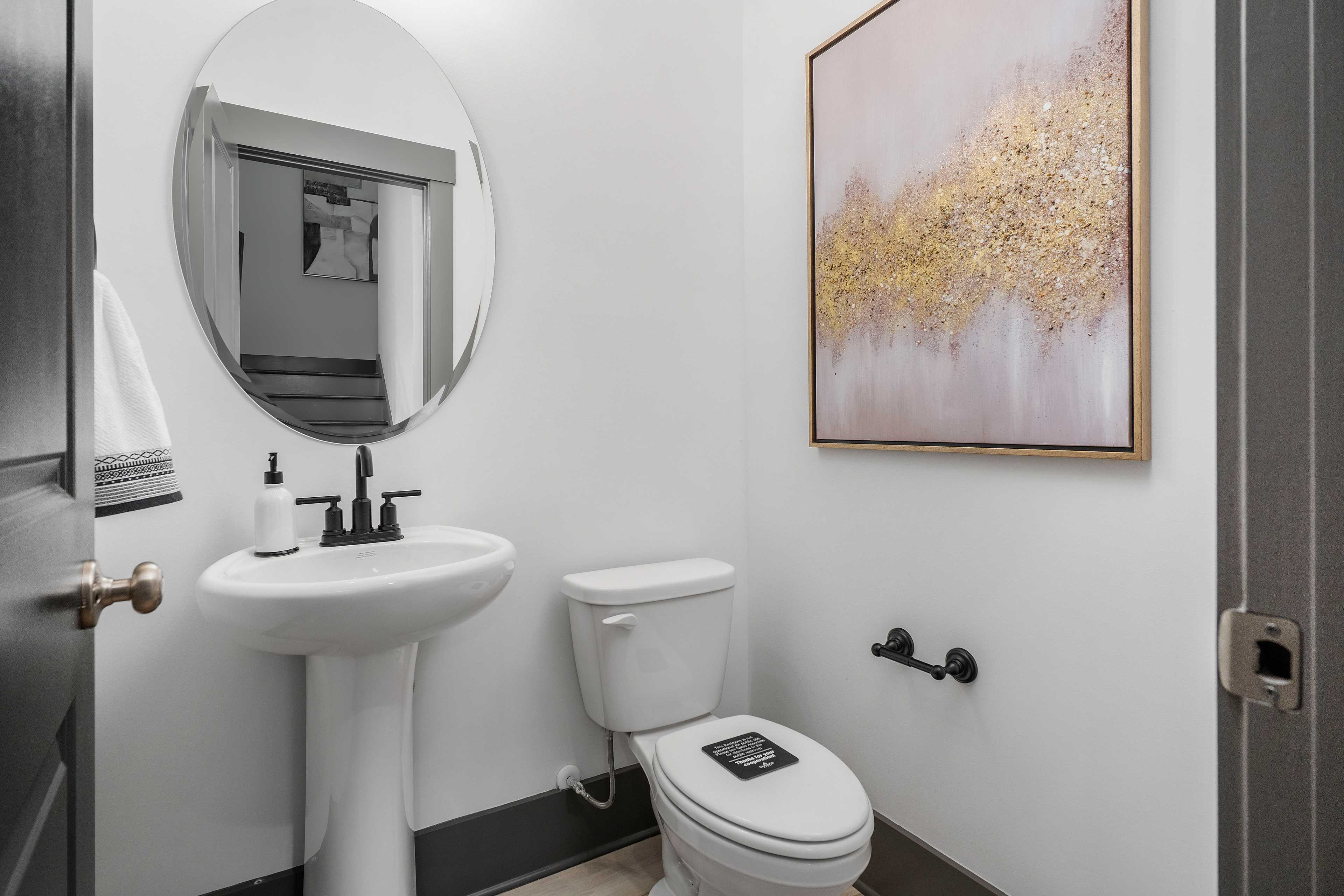 Elegant powder room at Barnett's Crossing in Madison, Alabama with white pedestal sink, round mirror, and abstract gold artwork