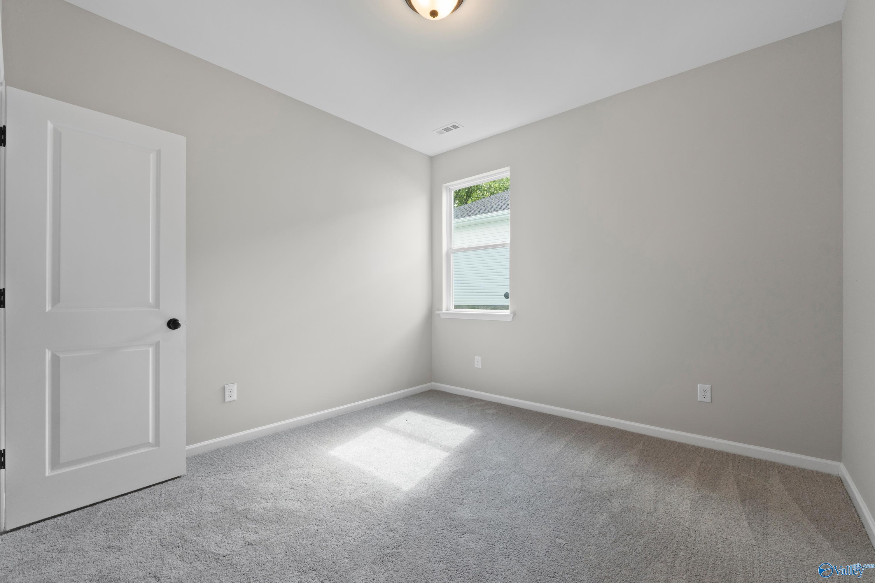 Sunlit empty bedroom with light gray walls, white paneled door, window blinds, and plush carpet in Davidson Homes The Phoenix, Fayetteville, TN