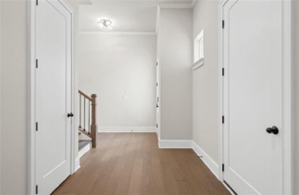 Bright open hallway with white doors, hardwood floors, and wooden staircase in Davidson Homes The Seaside A, Woodstock, GA