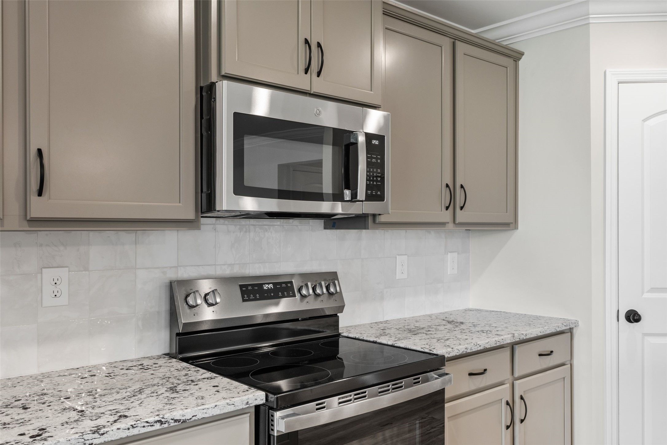 Modern kitchen with granite countertops, stainless steel appliances, and gray cabinets in The Holly C home, Anna, Texas.