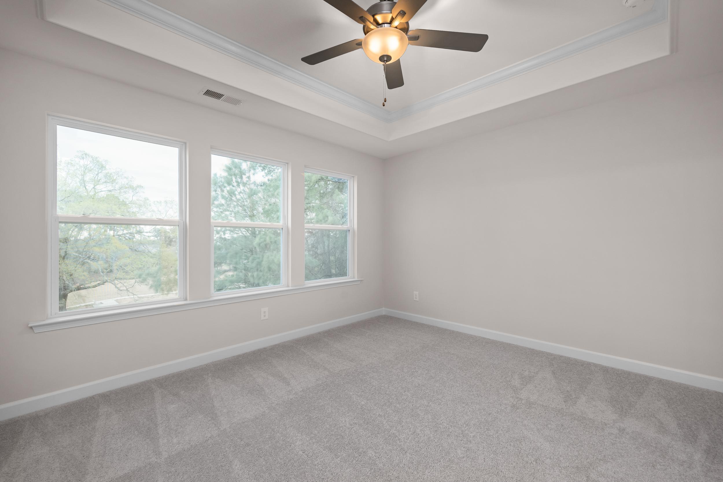 Spacious empty bedroom at Forestville Yard Townhomes in Knightdale NC with beige walls, carpet floor, ceiling fan and large tree-view windows