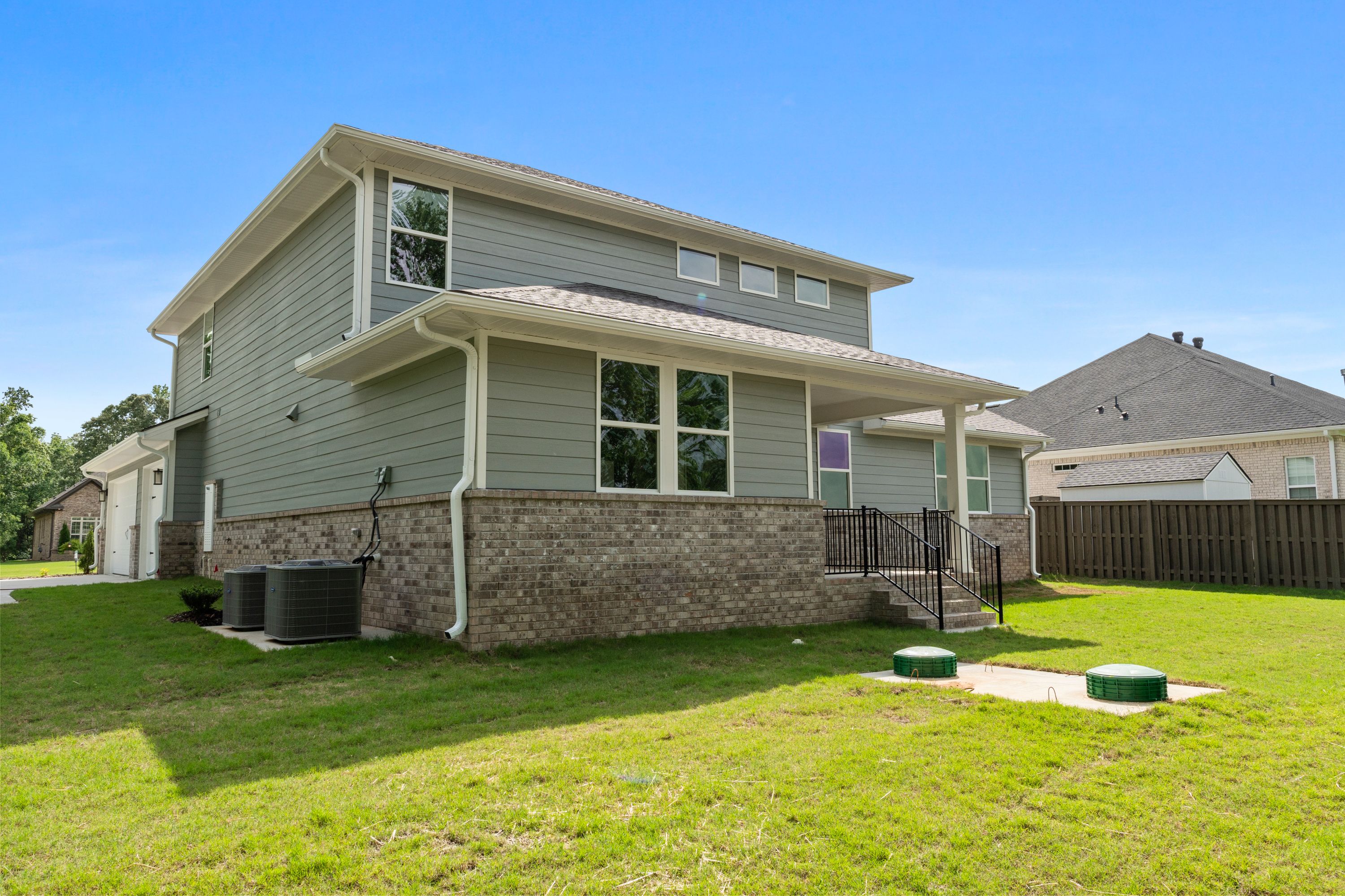 Two-story Avalon D home in Owens Cross Roads, Alabama, with gray siding, brick base, covered porch, 3-car garage, and lush green yard