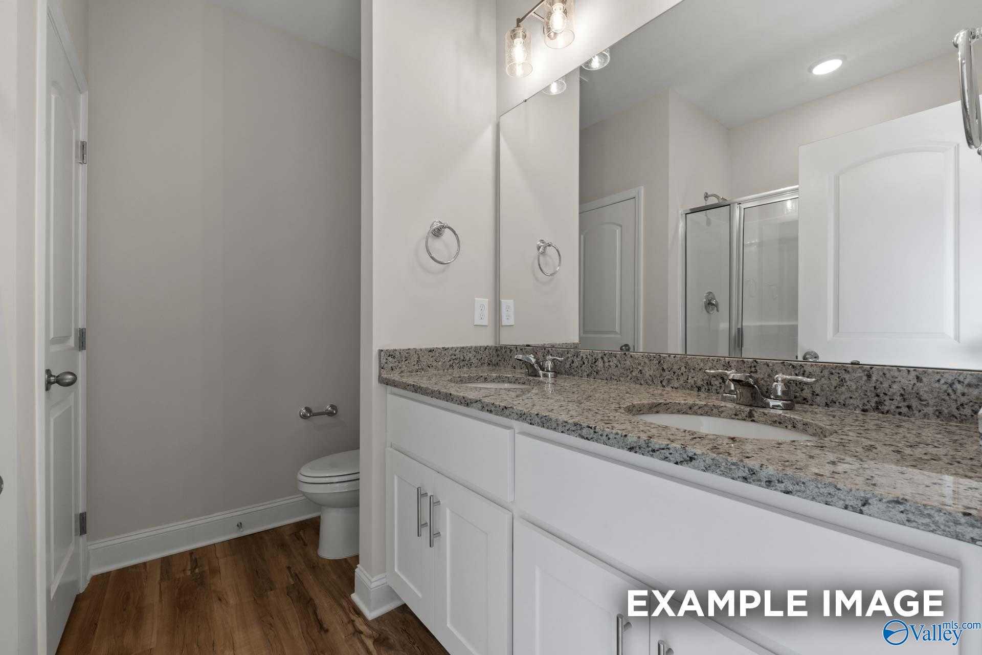 Modern bathroom featuring double granite vanity, frameless shower, and luxury vinyl plank flooring in Davidson Homes The Butler, Toney, AL