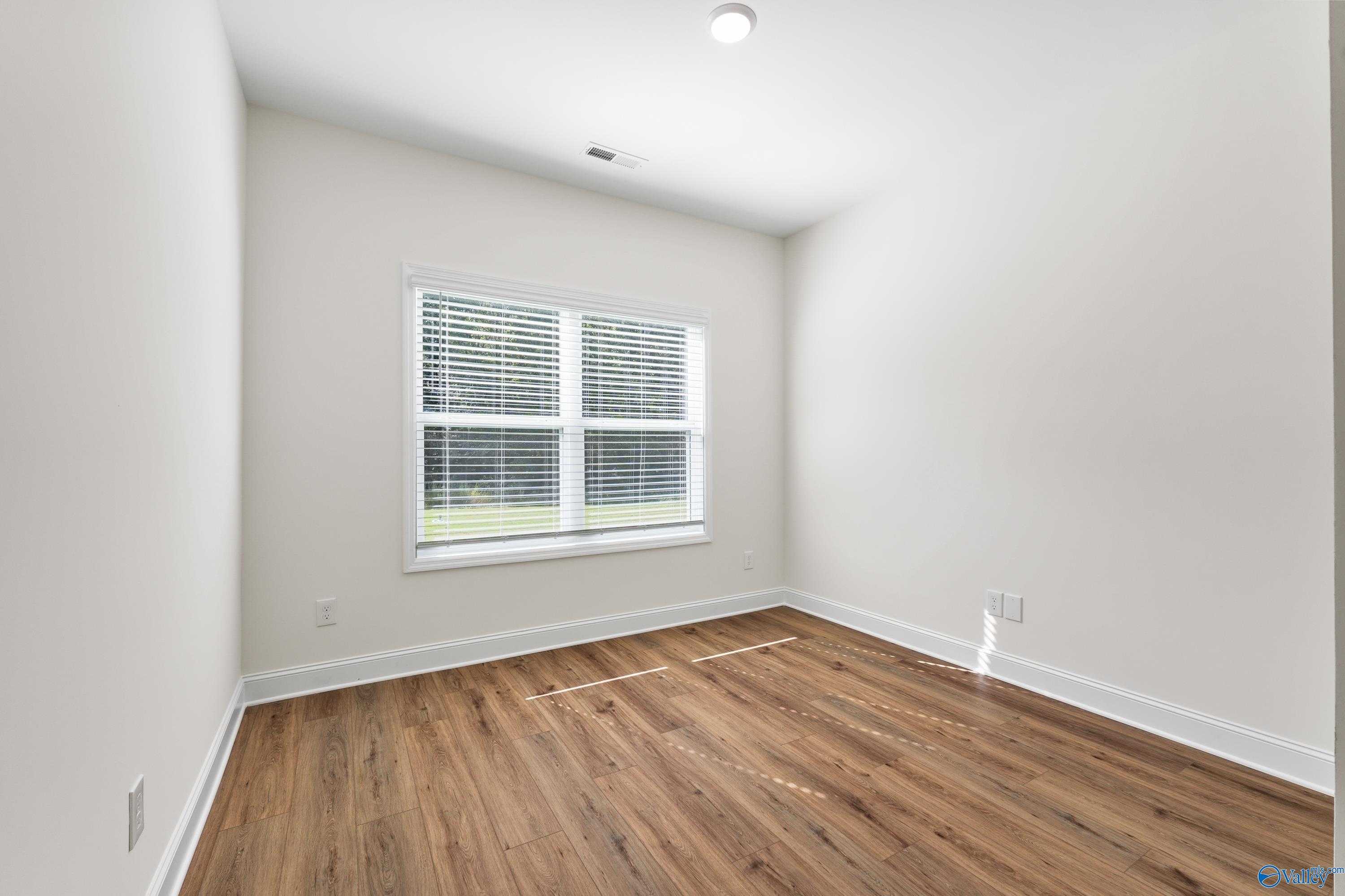 Bright secondary bedroom with hardwood floors, beige walls, and large window in Davidson Homes Shelby A, Athens, Alabama