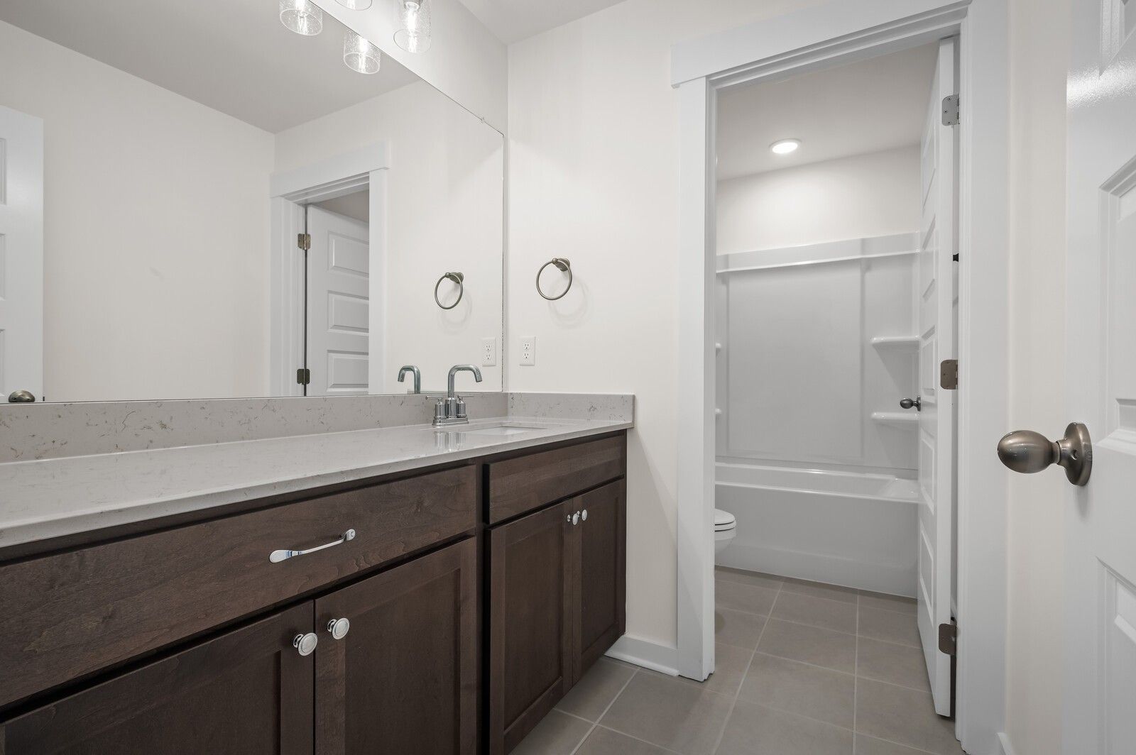 Modern bathroom with dark wood vanity, quartz countertop, and tub-shower combo in Woods Crossing, Gallatin, Tennessee home.