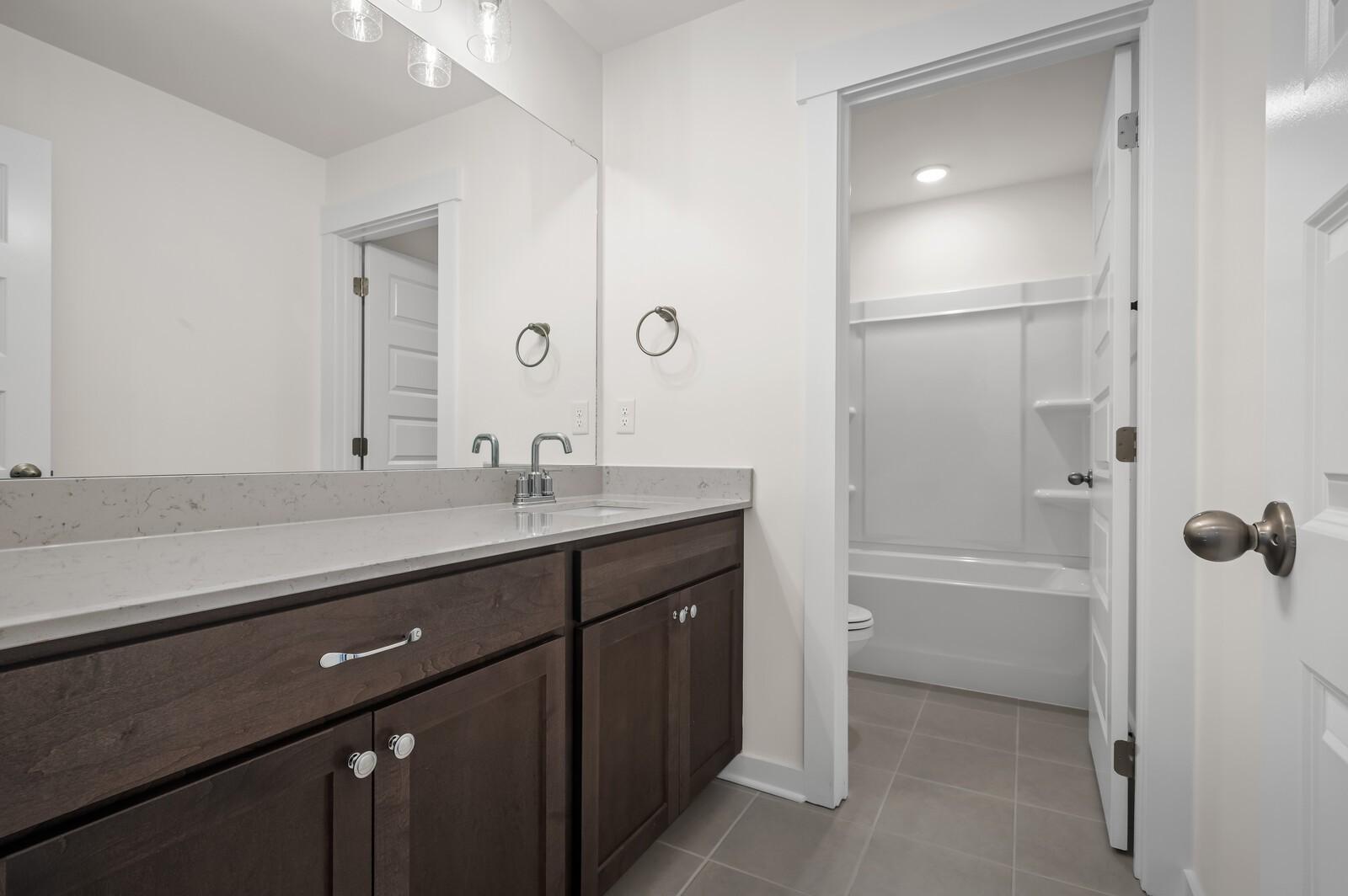 Modern bathroom with dark wood vanity, quartz countertop, and tub-shower combo in Woods Crossing, Gallatin, Tennessee home.