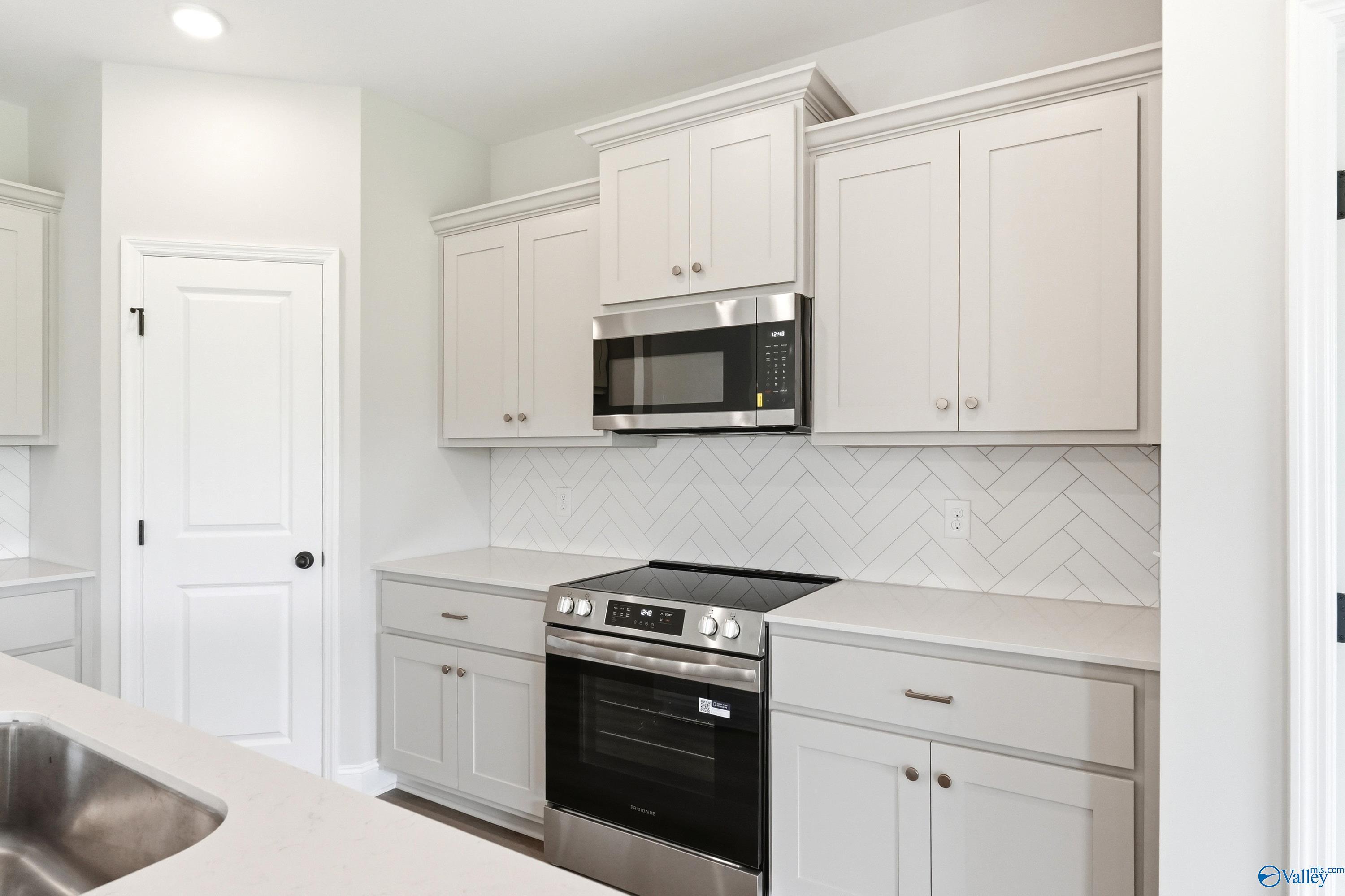Modern kitchen with white shaker cabinets, herringbone tile backsplash, and stainless appliances in The Franklin floor plan.