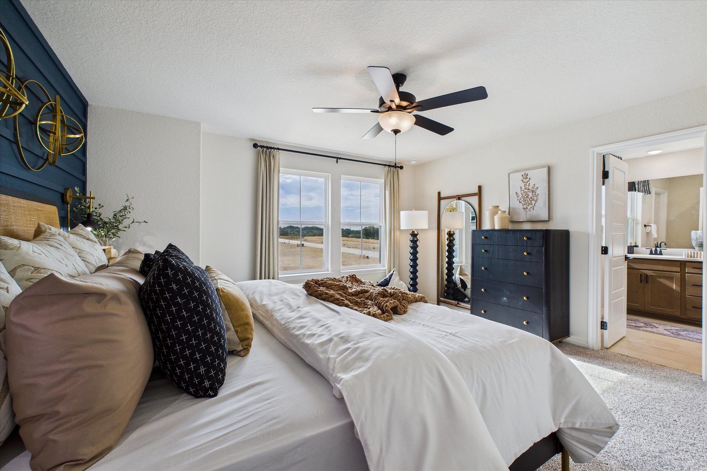 Spacious master bedroom at Meadows at Oak Creek in San Antonio Texas with navy accent wall, plush king bed, ceiling fan, and en-suite bath
