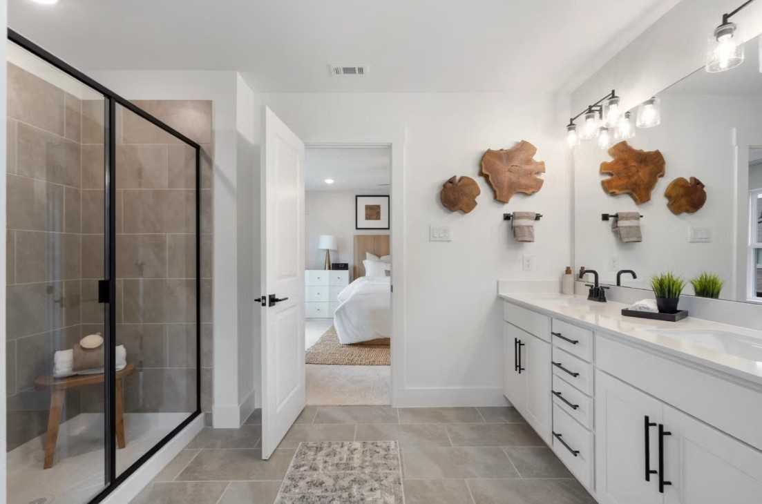 Modern master bathroom featuring frameless glass shower, double white vanity, wood wall art in Davidson Homes The Wake C, Wylie, Texas