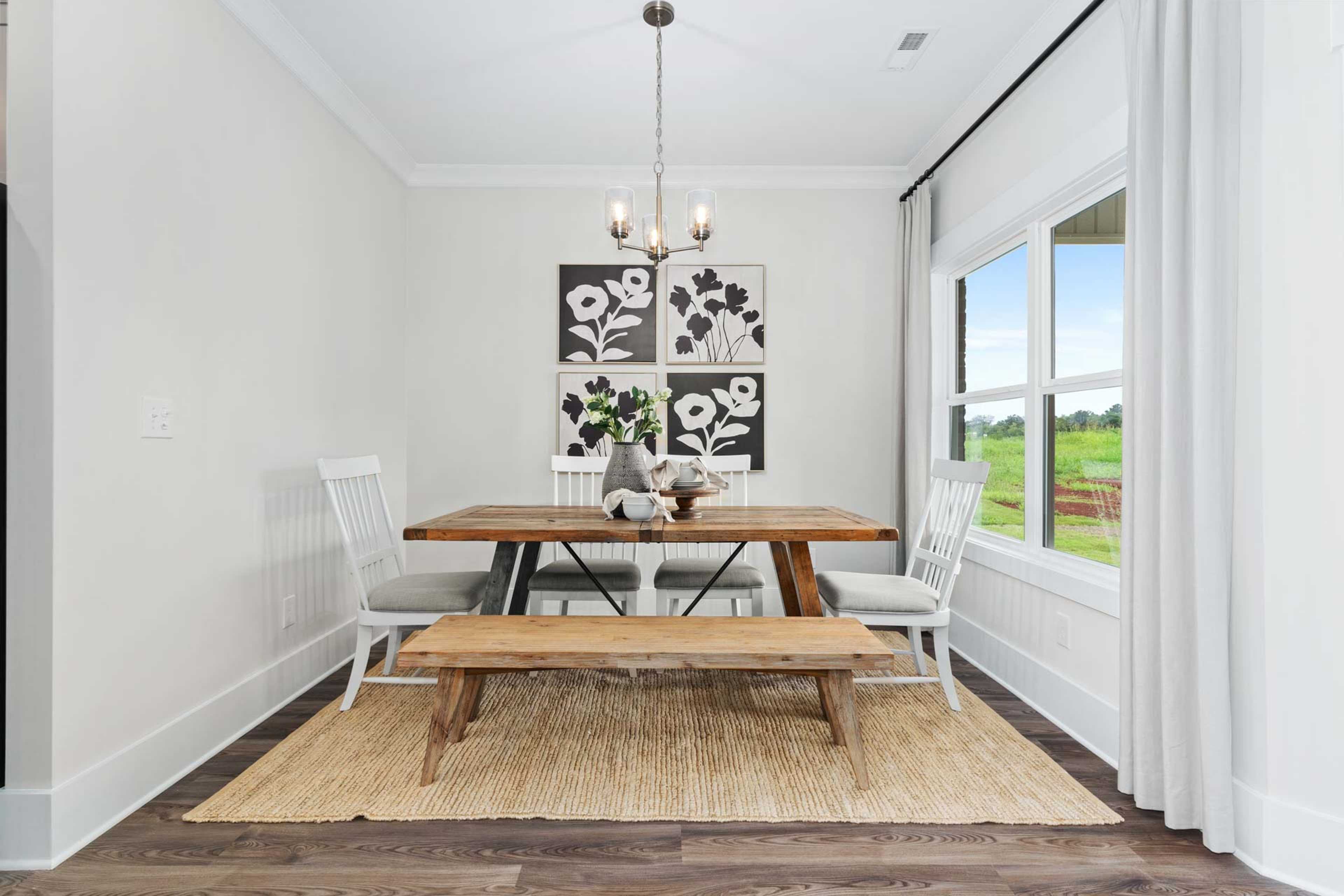 Rustic dining room at The Meadows in Athens AL with wooden table, benches, floral wall art, chandelier, and large windows