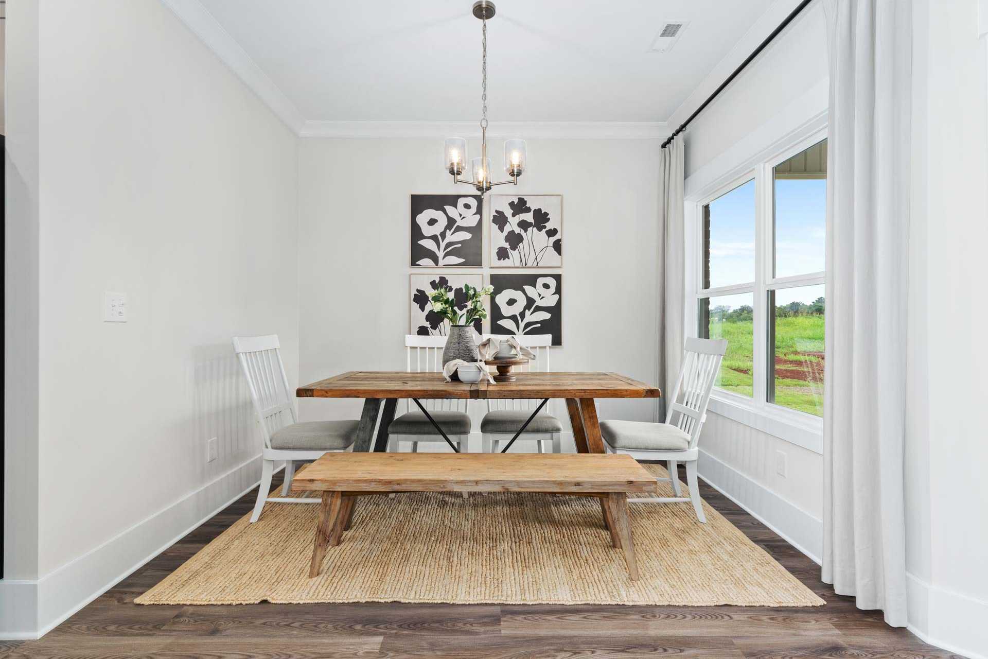 Rustic dining room at The Meadows in Athens AL with wooden table, benches, floral wall art, chandelier, and large windows