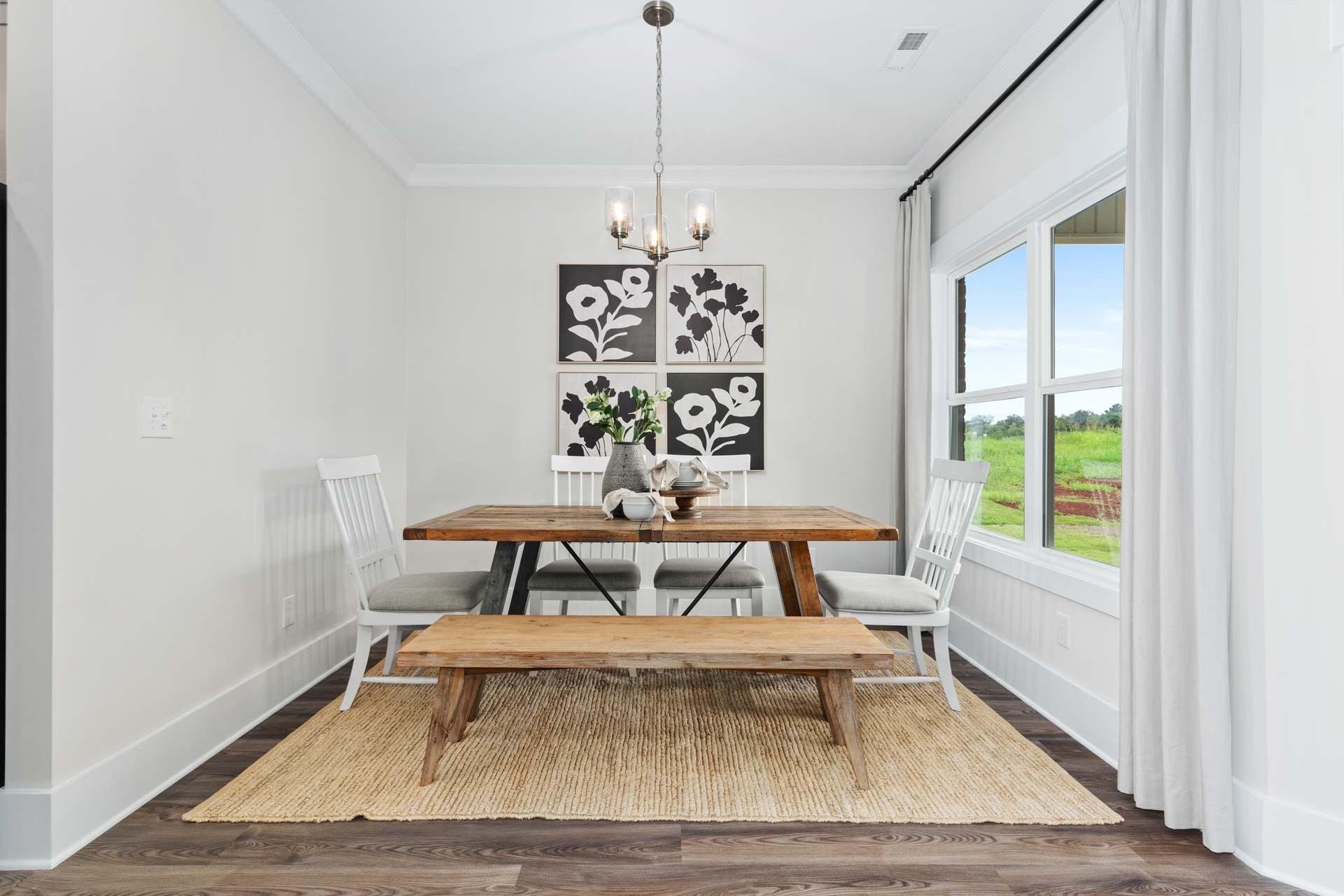 Rustic dining room at The Meadows in Athens AL with wooden table, benches, floral wall art, chandelier, and large windows