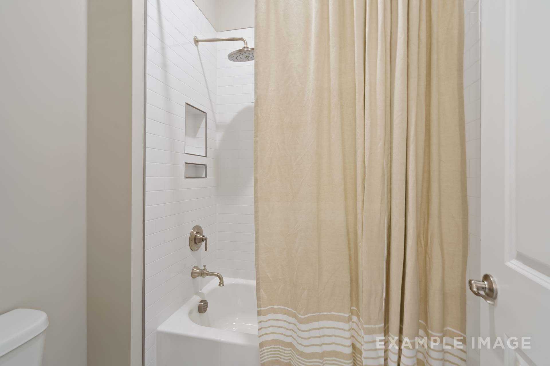 Spacious bathroom in The Seaside home with white tiled bathtub shower, beige curtain, and chrome fixtures