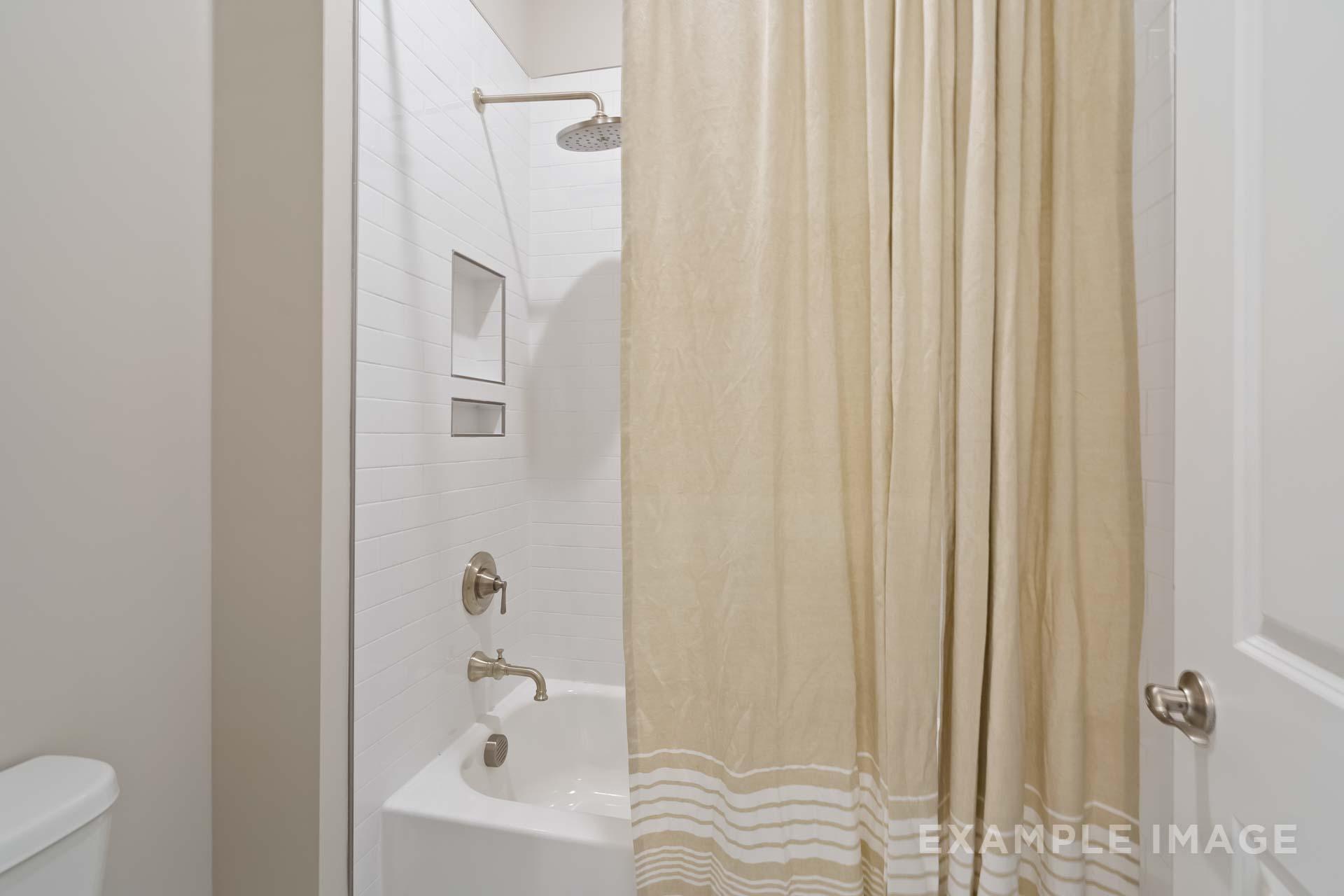 Spacious secondary bathroom in The Seaside C by Davidson Homes featuring white tiled shower, oval bathtub, and beige curtain