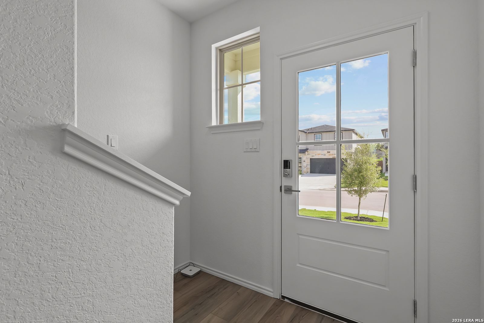 Bright entryway with glass-paneled front door and wood-style flooring in The Brazos B home in Agave, San Antonio, Texas.