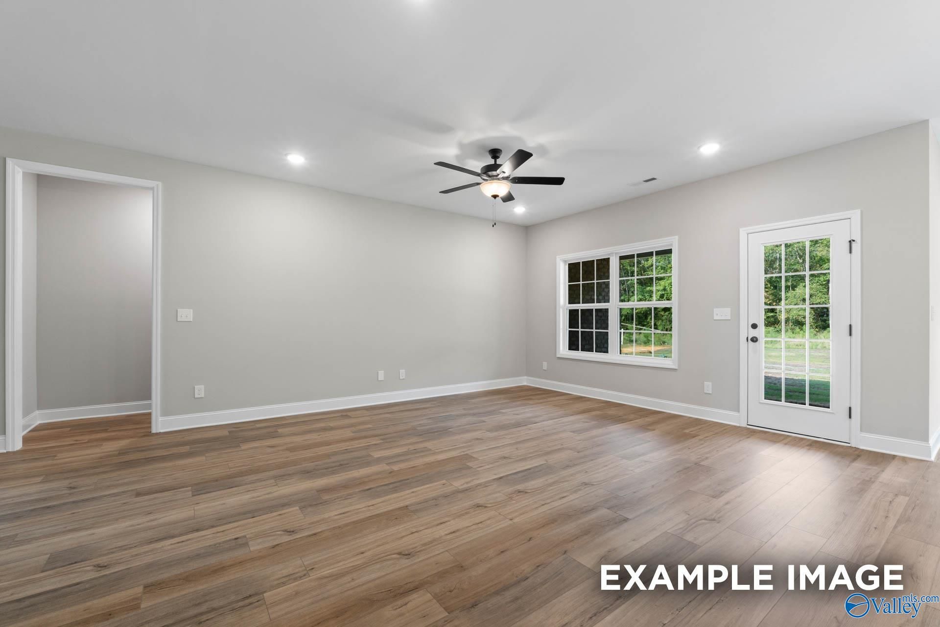 Bright living room with hardwood floors, ceiling fan, large windows, and French doors to backyard in 3-bedroom Montgomery B home, Toney, Alabama