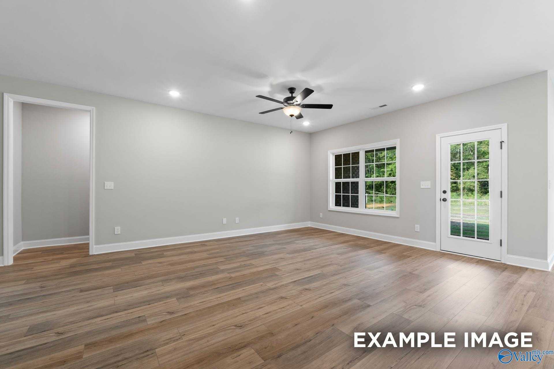 Bright living room with hardwood floors, ceiling fan, large windows, and French doors to backyard in 3-bedroom Montgomery B home, Toney, Alabama