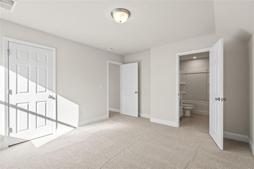 Bright secondary bedroom with attached bath and open doors in Davidson Homes The Ash C at Wehunt Meadows, Hoschton, Georgia