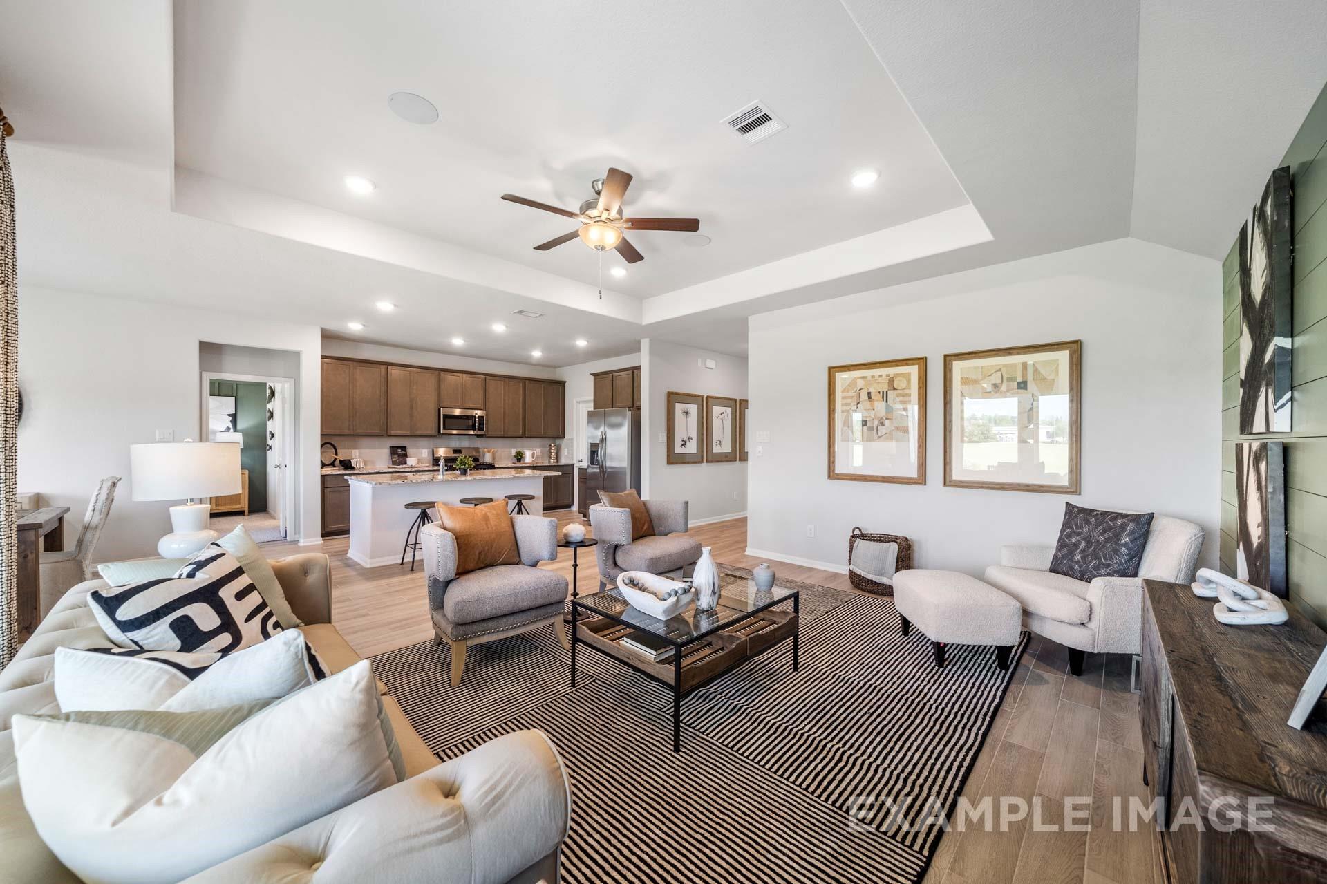 Open-concept living room with tray ceiling and ceiling fan overlooking kitchen in The Acadia A floor plan, Lago Mar, Texas City