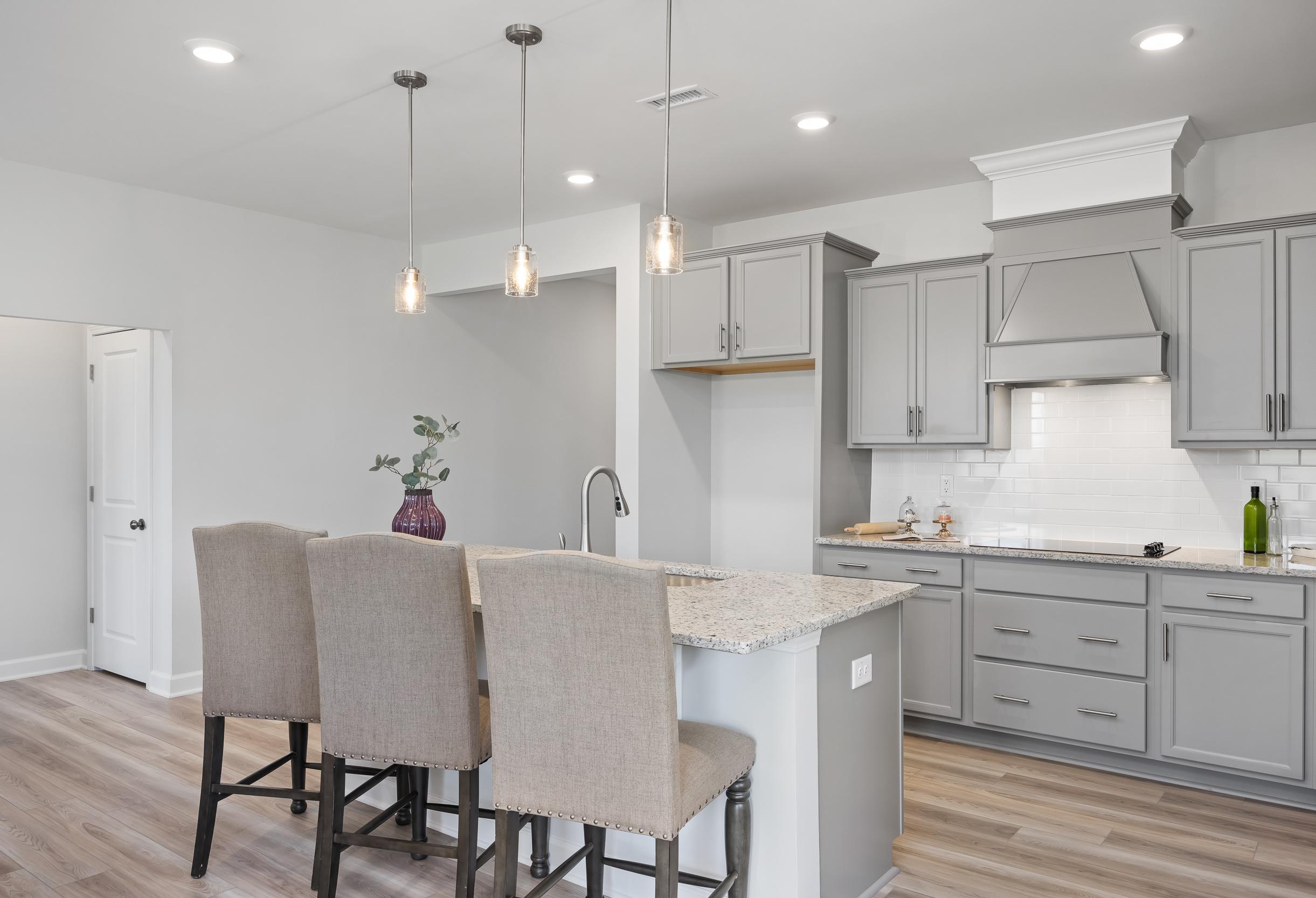 Spacious kitchen in The Daphne C featuring gray shaker cabinets, quartz island with bar stools, and pendant lights