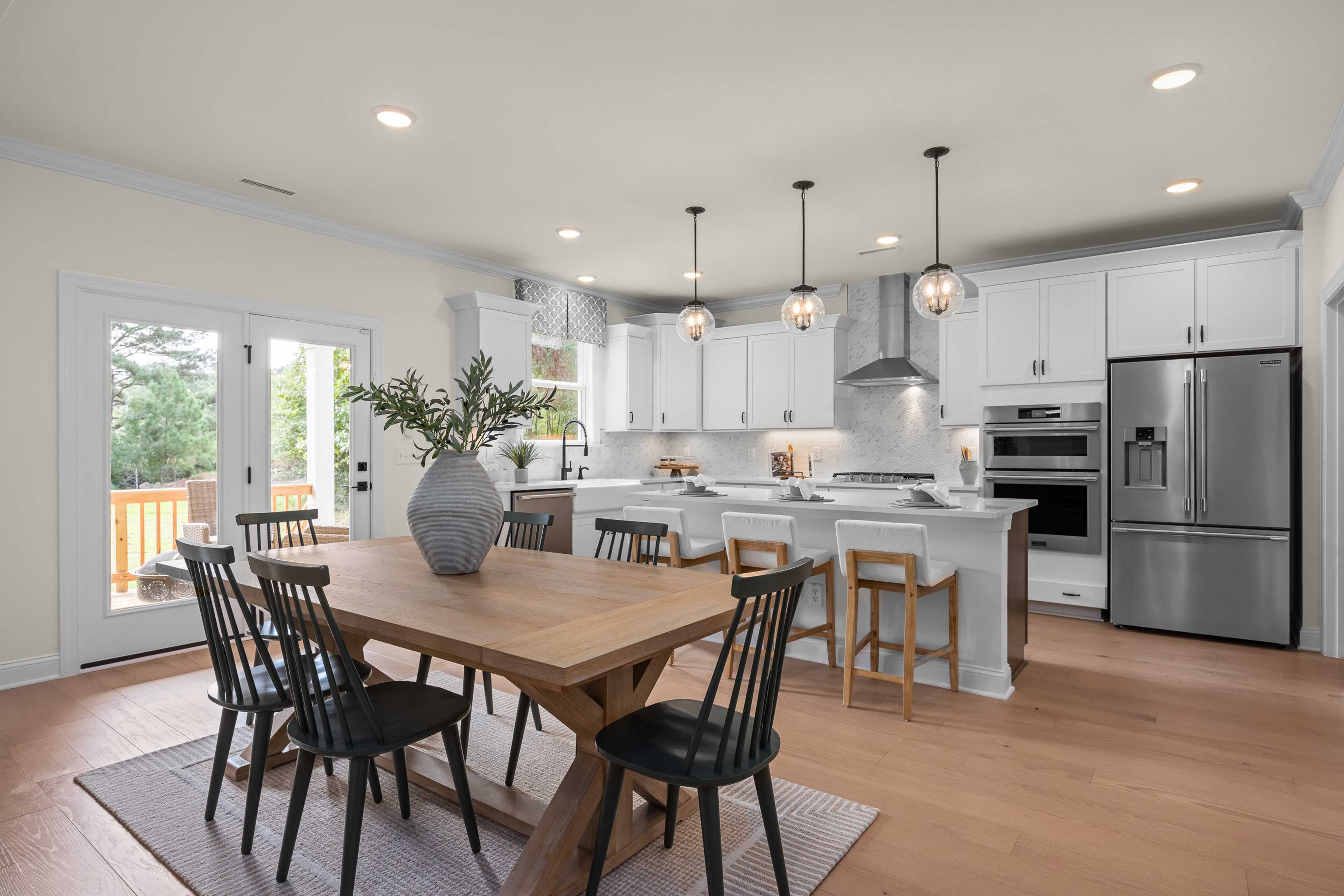 Spacious open-concept kitchen at Laneridge Estates in Raleigh NC with white cabinets, stainless appliances, island bar, and wooden dining table