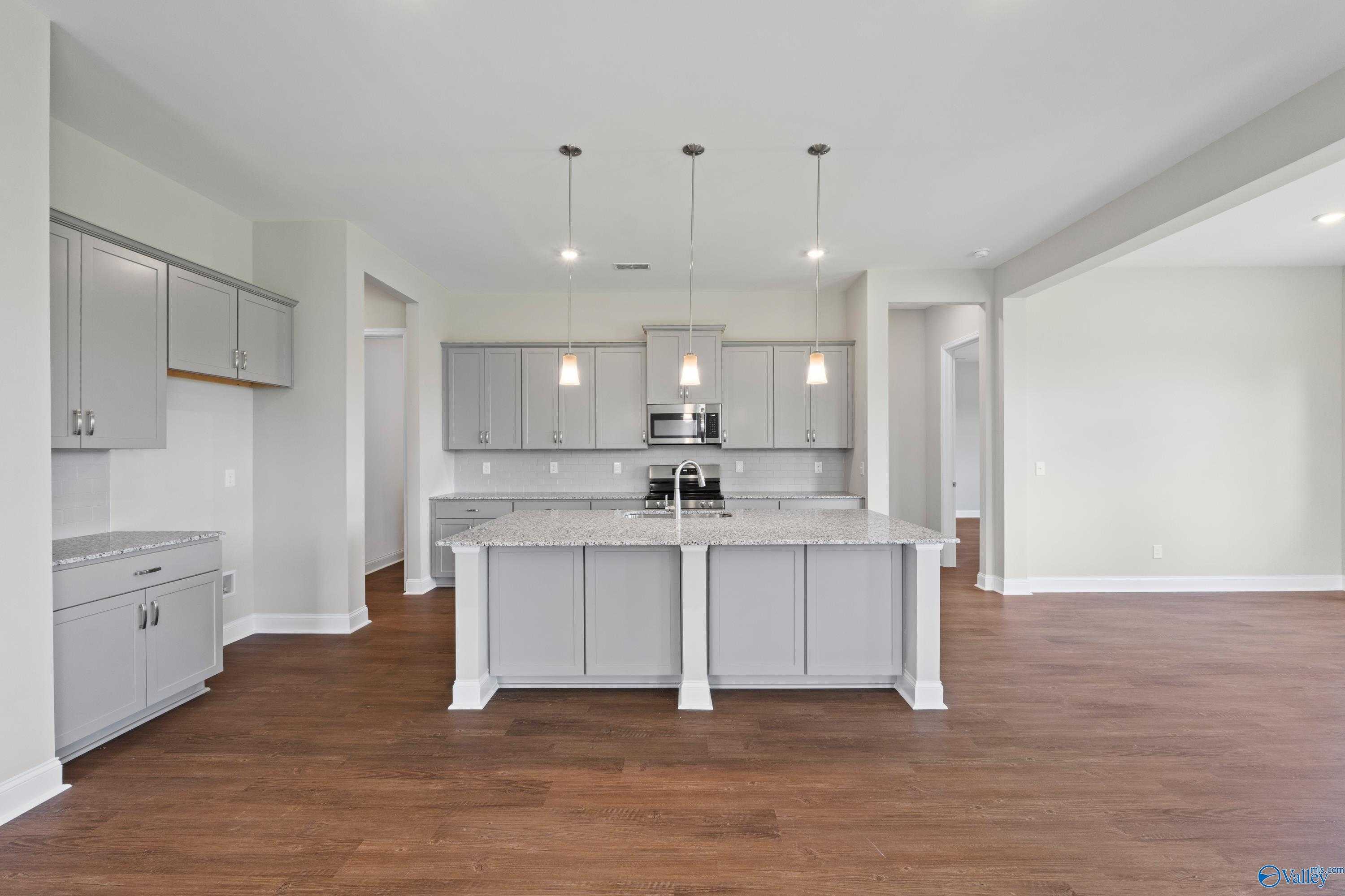 Modern gray kitchen with large center island, stainless steel appliances, and pendant lights in Davidson Homes The Arcadia, Huntsville, AL