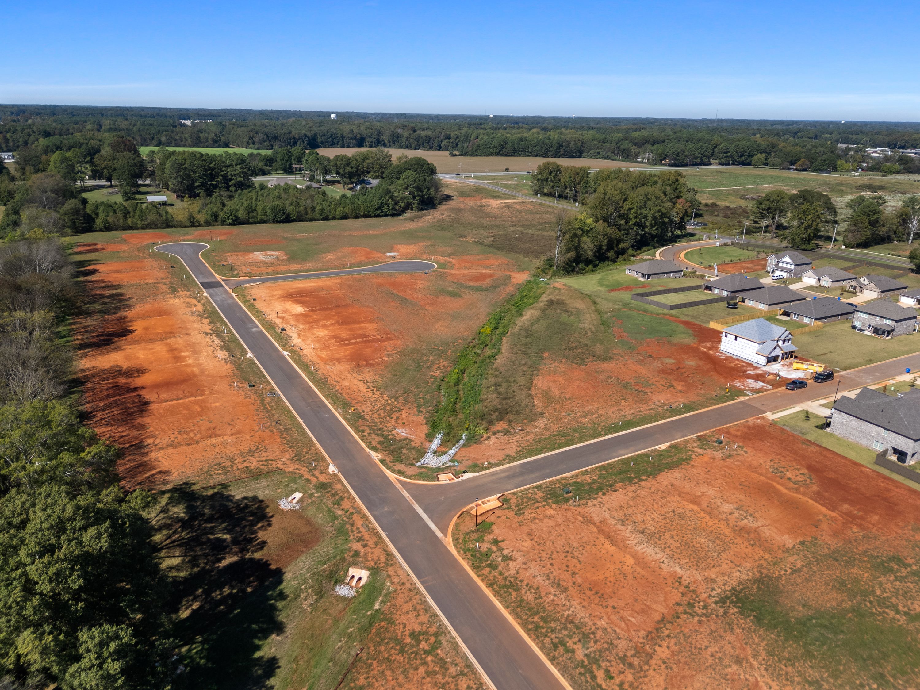 Aerial view of new homes and red dirt lots at The Meadows in Athens Alabama by Davidson Homes with paved roads and trees