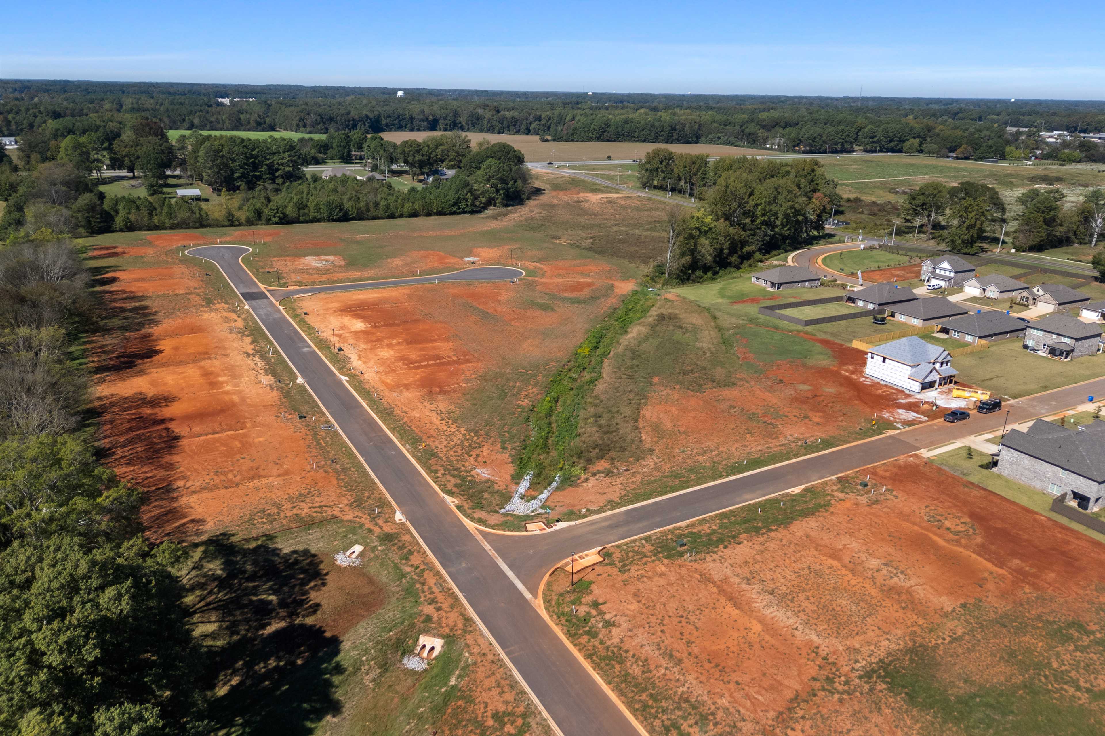 Aerial view of new homes and red dirt lots at The Meadows in Athens Alabama by Davidson Homes with paved roads and trees