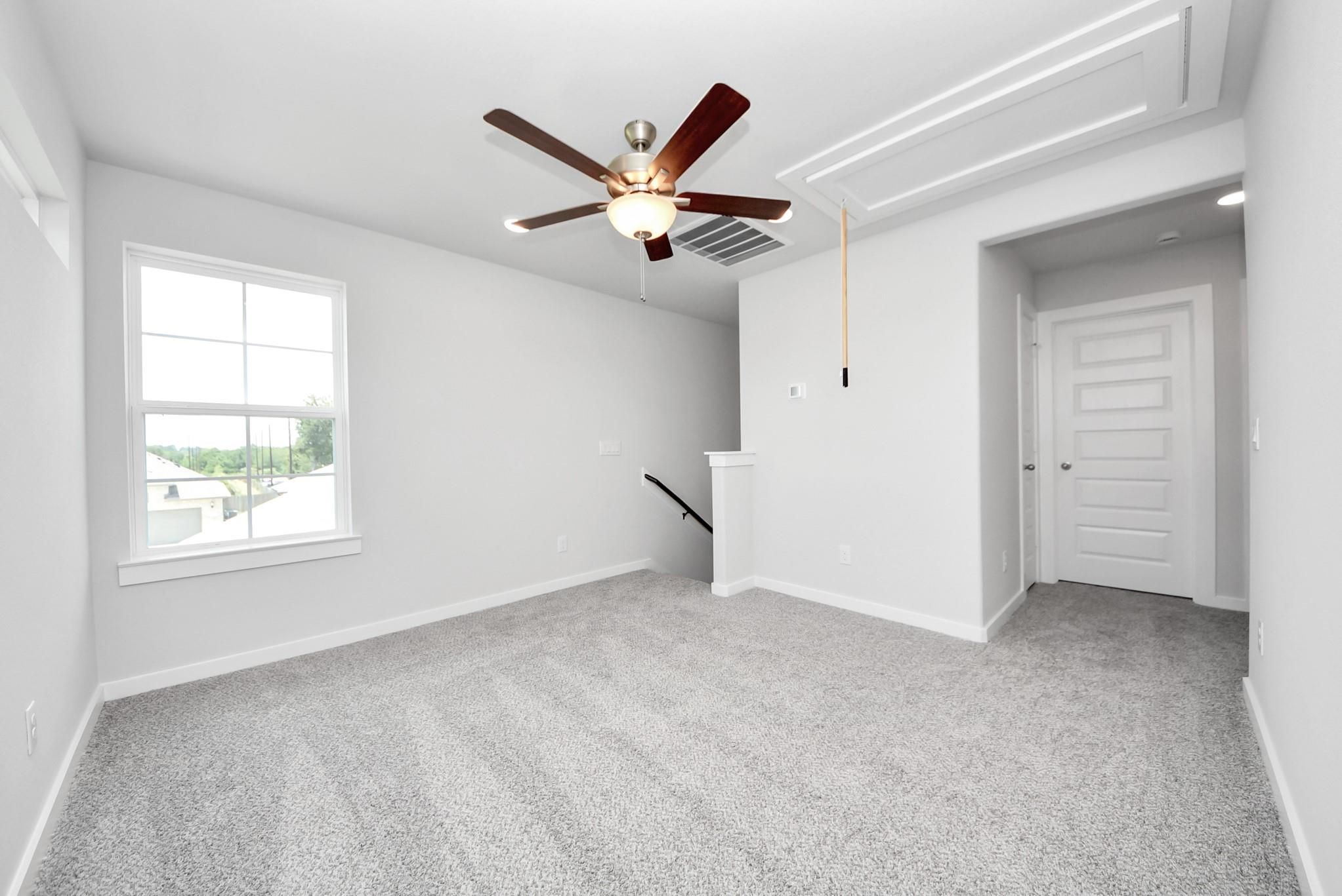 Spacious carpeted upstairs game room with ceiling fan in The Sabine E floor plan by Davidson Homes in Magnolia, Texas.