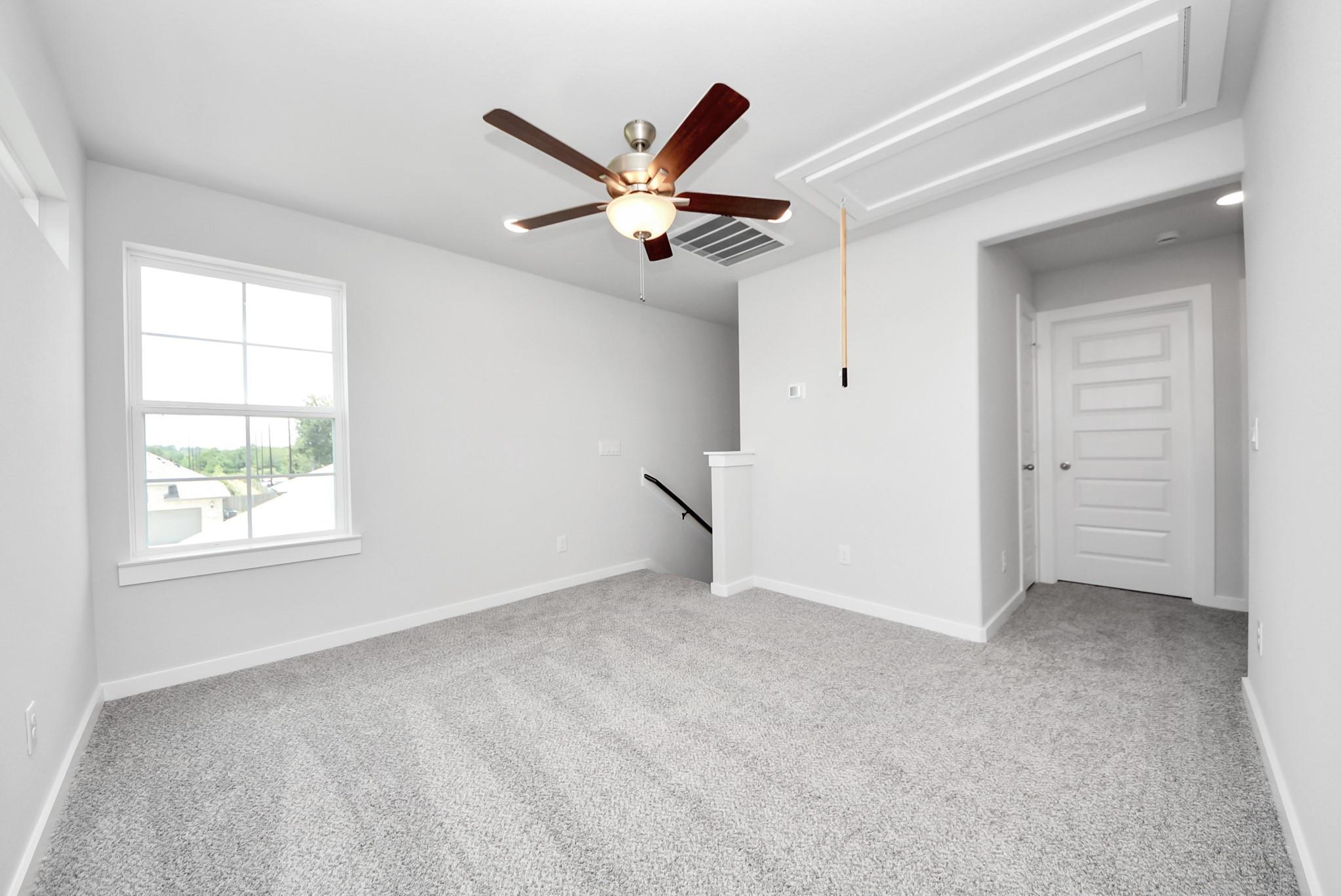 Spacious carpeted upstairs game room with ceiling fan in The Sabine E floor plan by Davidson Homes in Magnolia, Texas.