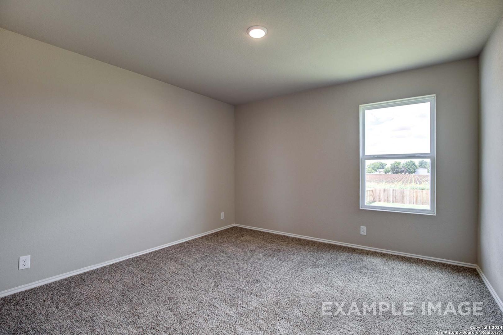 Spacious empty bedroom with neutral beige walls, carpet flooring, and window overlooking backyard in Davidson Homes The Murray J, Bricewood, San Antonio