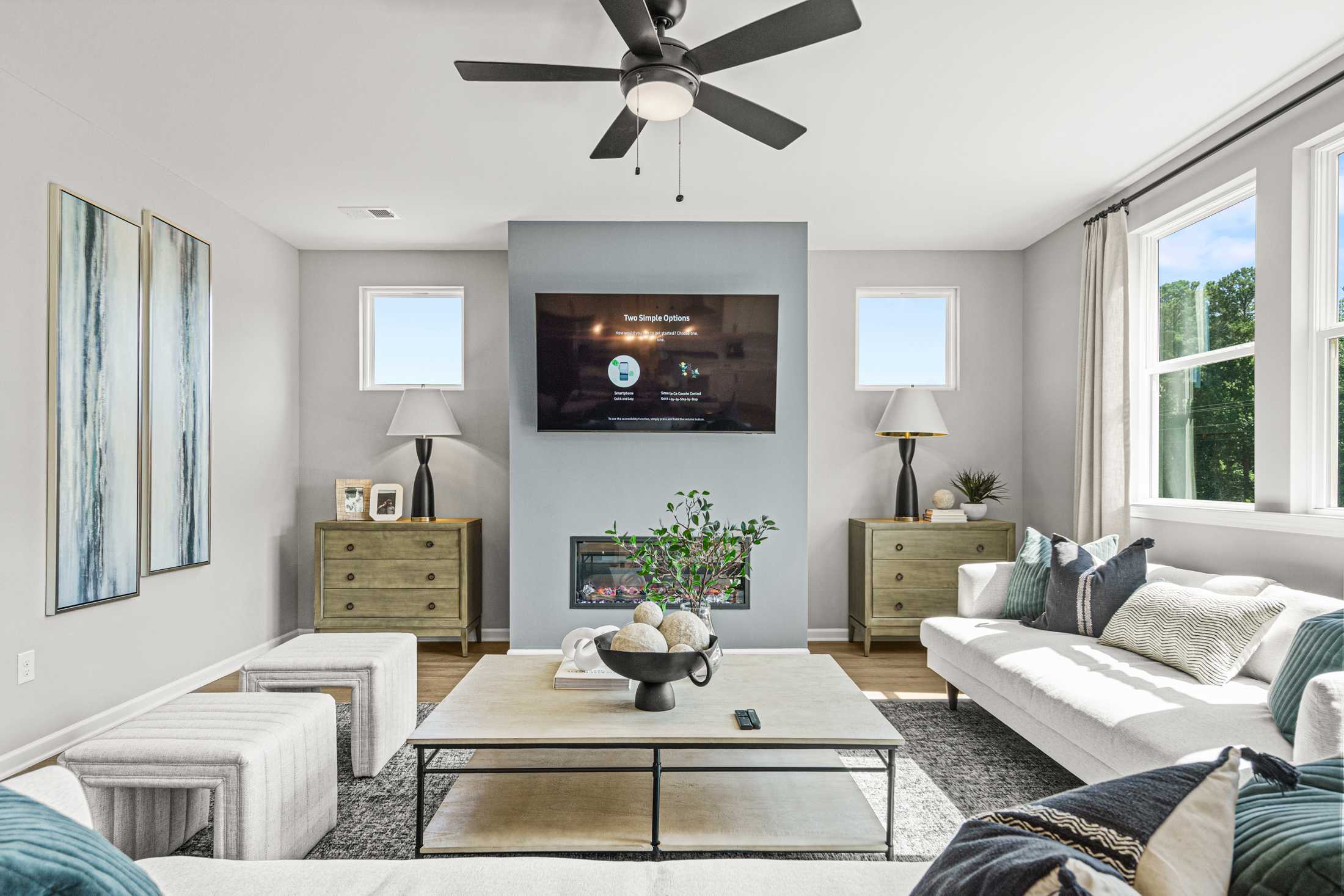 Spacious living room at Cedar Farms in Winder GA featuring gray accent wall with fireplace, mounted TV, white sofa, hardwood floors, and large windows