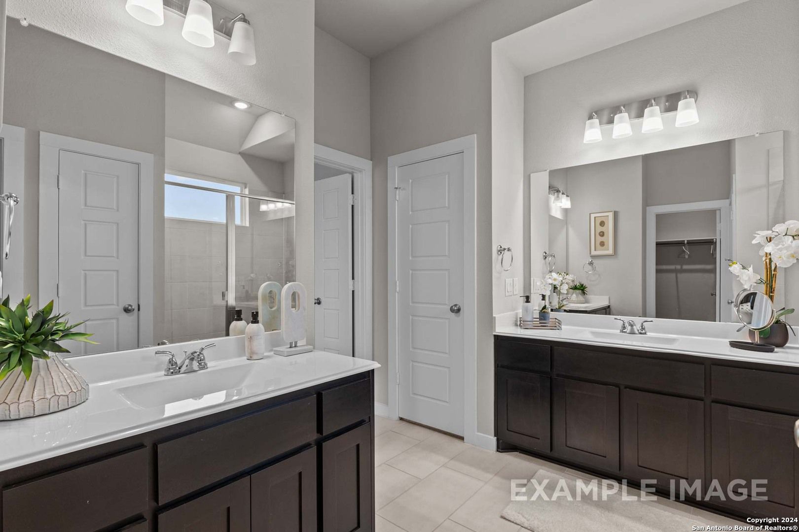Elegant master bathroom featuring double vanity sinks, large mirrors, and dark wood cabinets in Davidson Homes The Collin A, Seguin, Texas