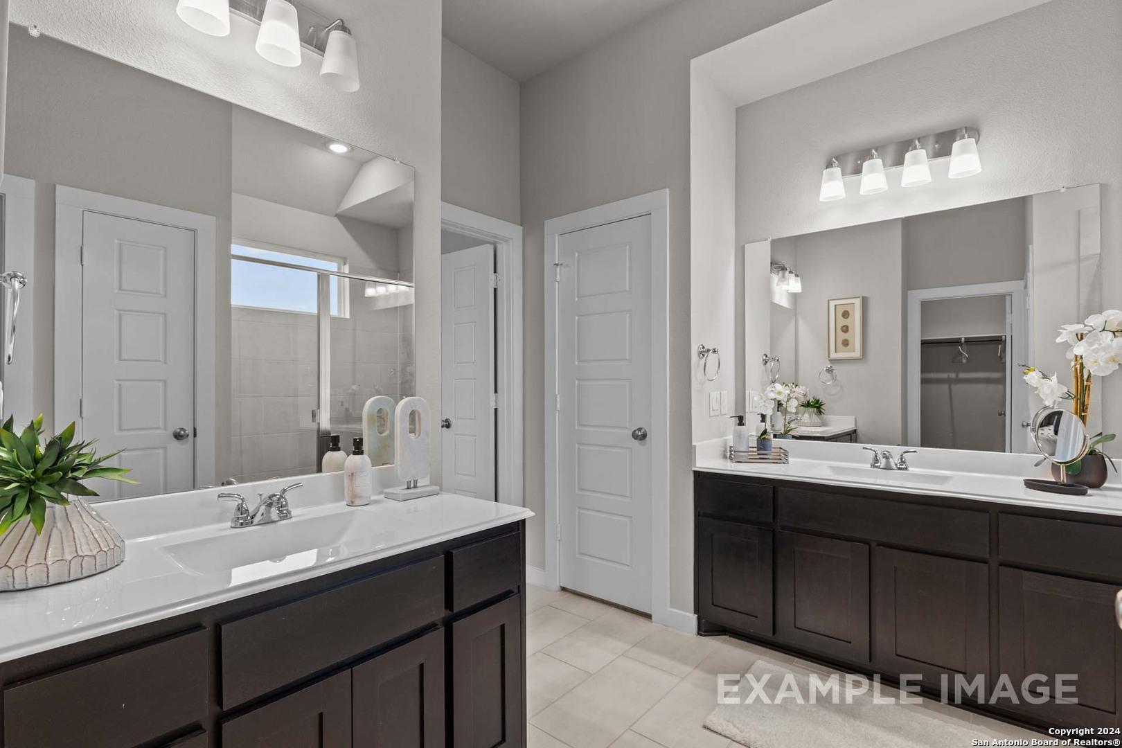 Elegant master bathroom featuring double vanity sinks, large mirrors, and dark wood cabinets in Davidson Homes The Collin A, Seguin, Texas